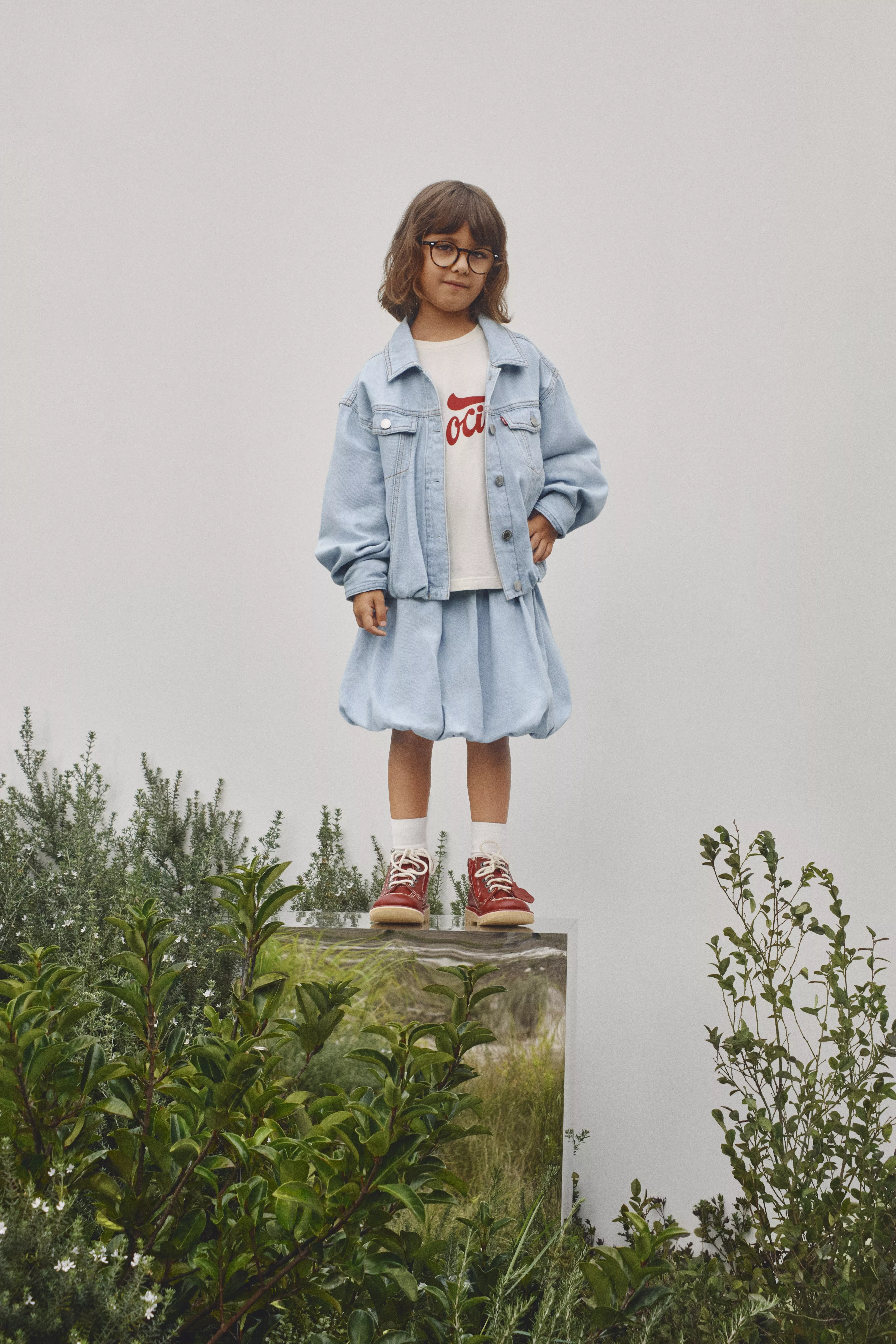 girl wearing light blue denim jacket and skirt with red trainers