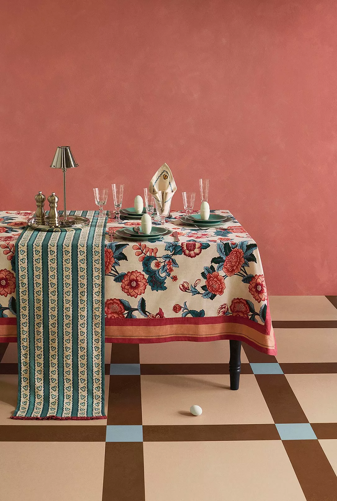 Elegant interior with blue lamp, white shade, floral arrangement on textured table, and teal sofa. Earthy wall art.