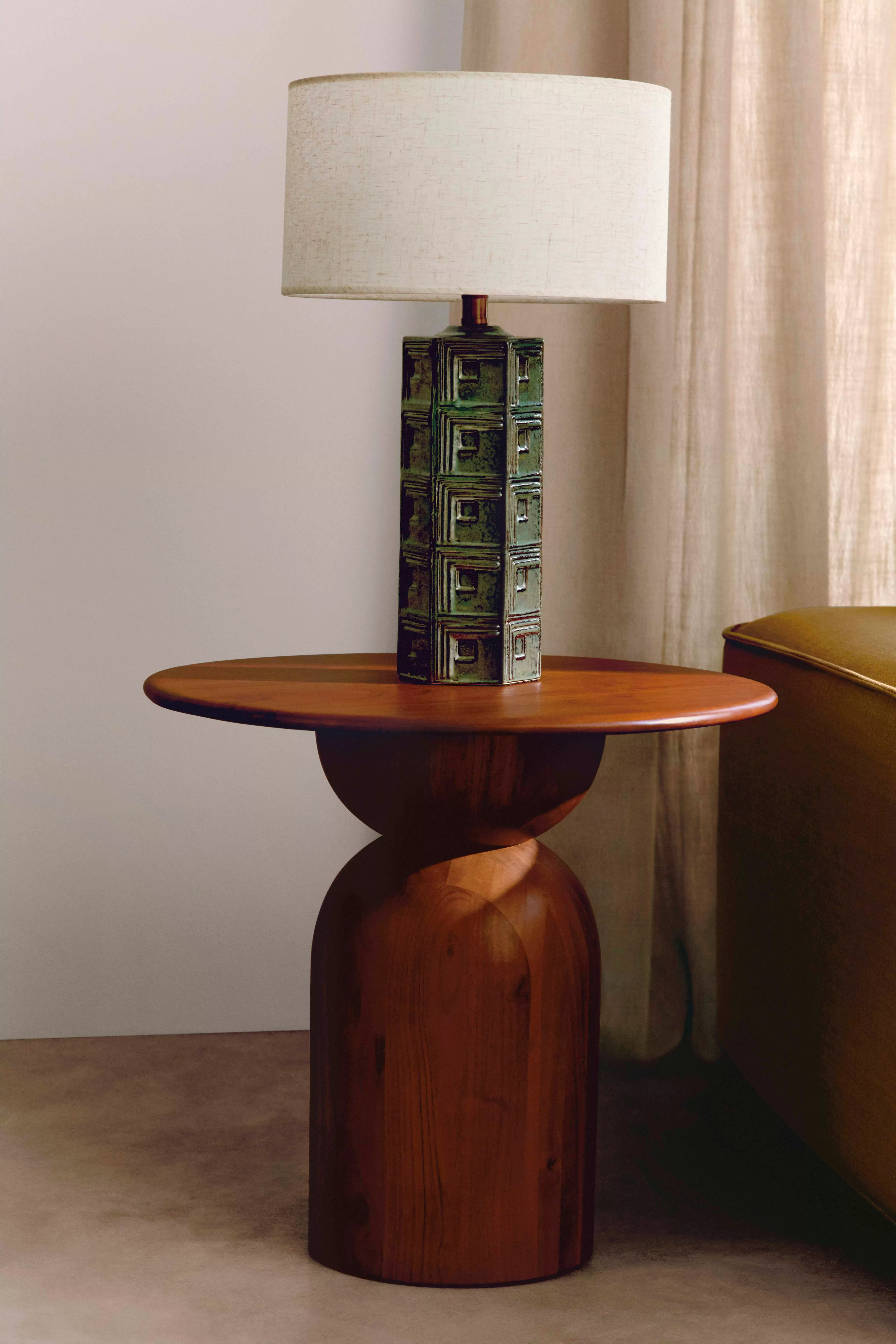 Elegant wooden side table with a textured lamp and neutral lampshade, set against beige curtains.