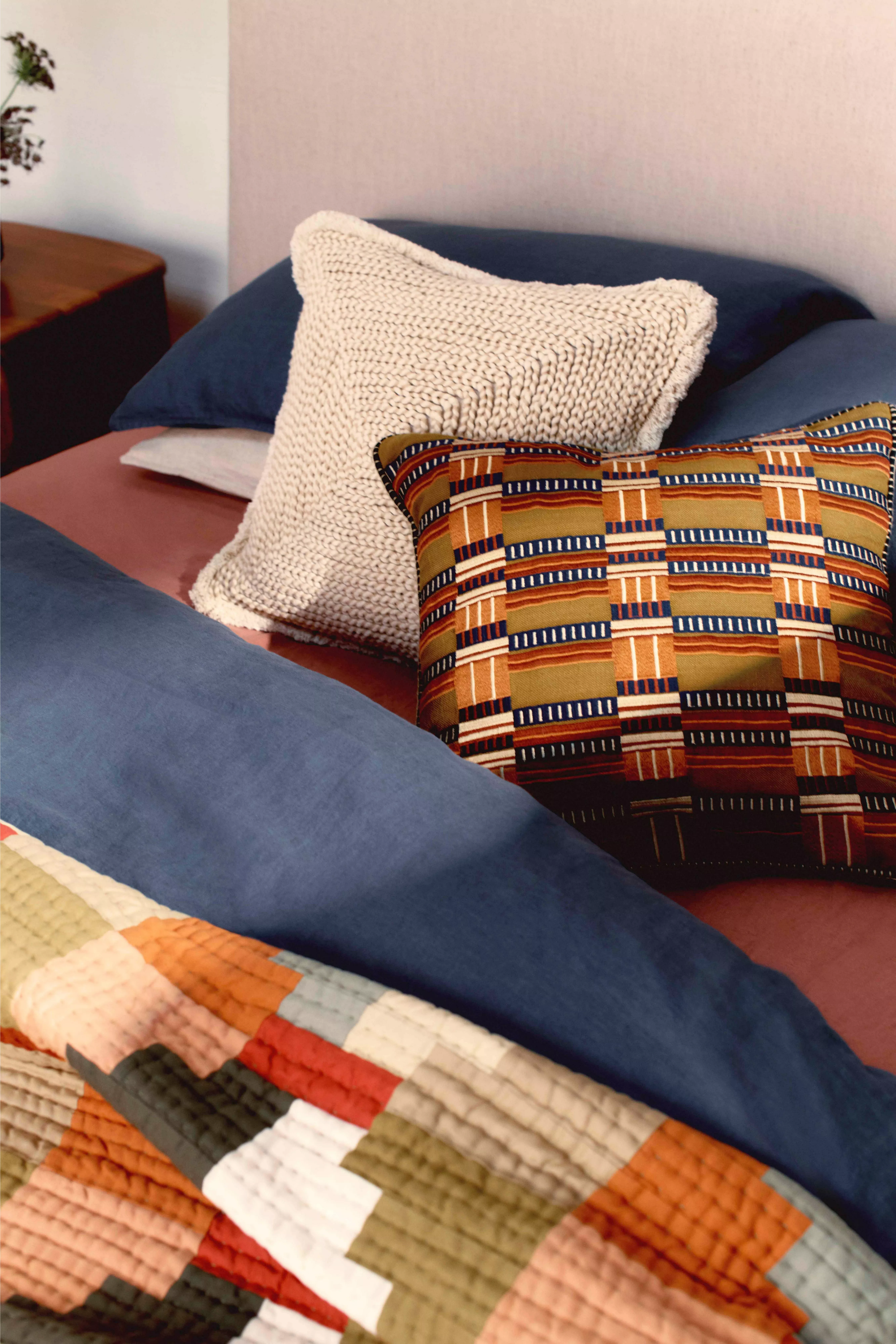 Cosy bedroom decor featuring a textured cream pillow, a colourful patterned cushion, and a patchwork quilt.