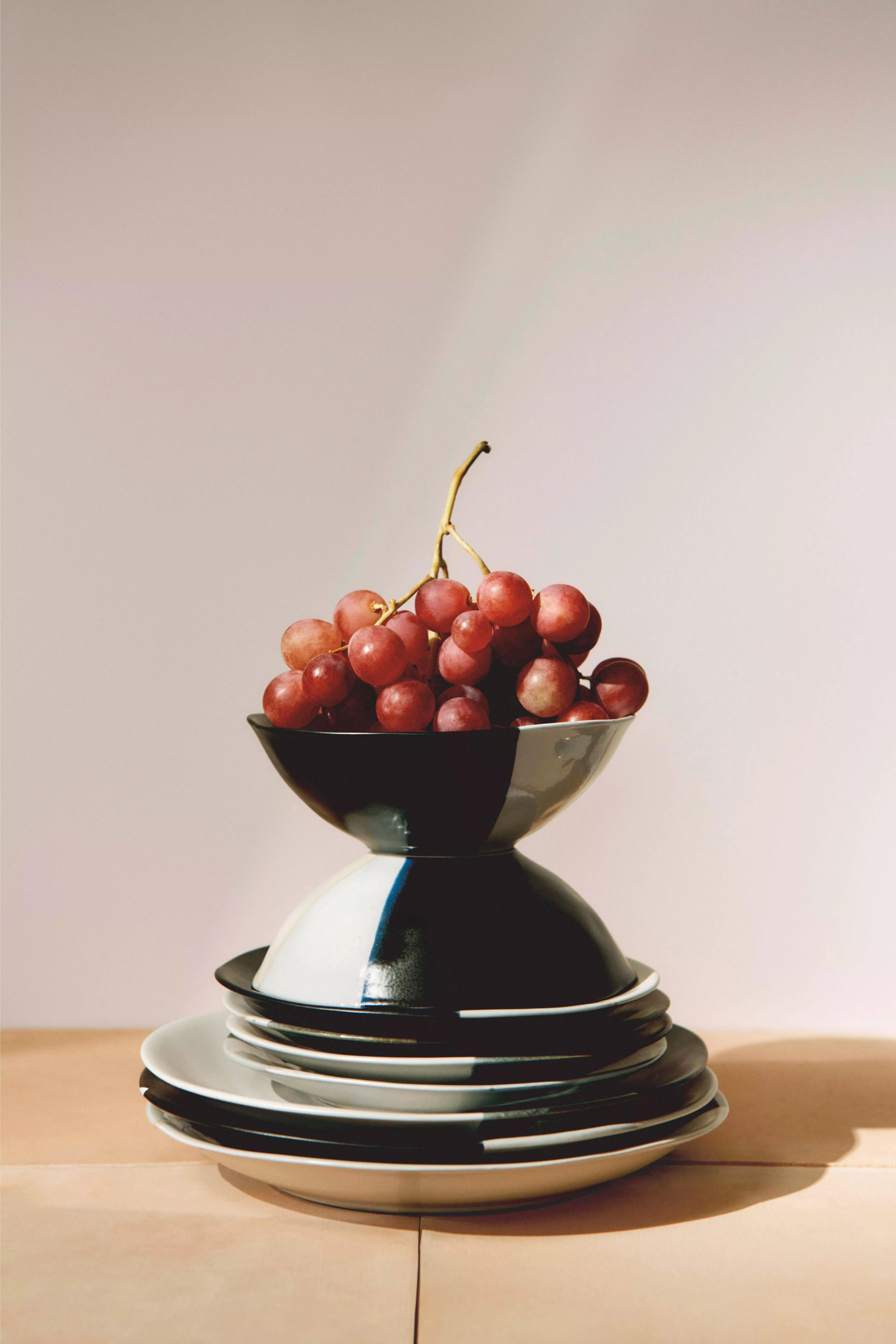 A stack of plates topped with a bowl of red grapes, elegantly arranged in natural light.