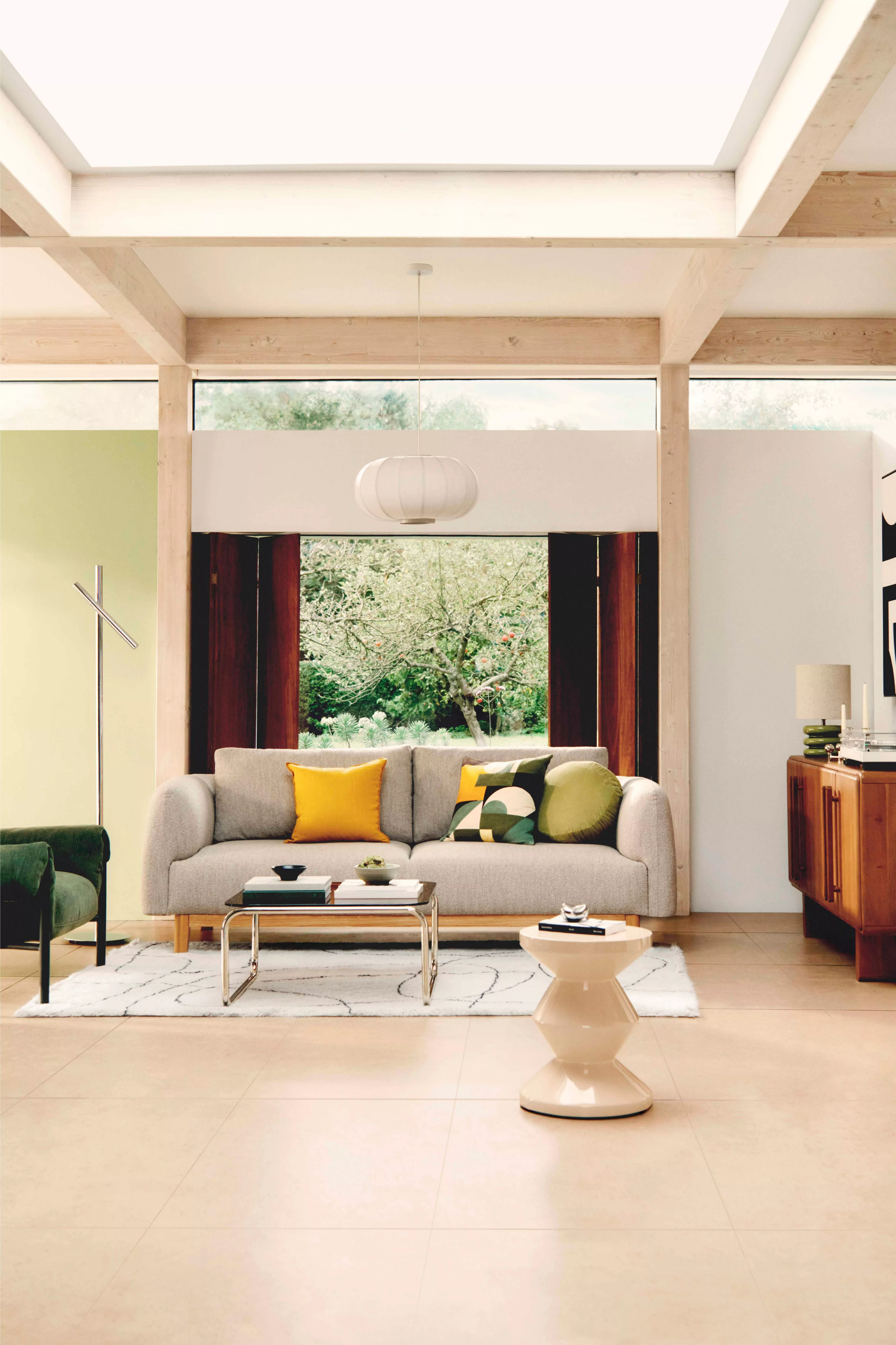 Modern living room with large window, beige sofa and colourful cushions. Wooden furniture and stylish decor.