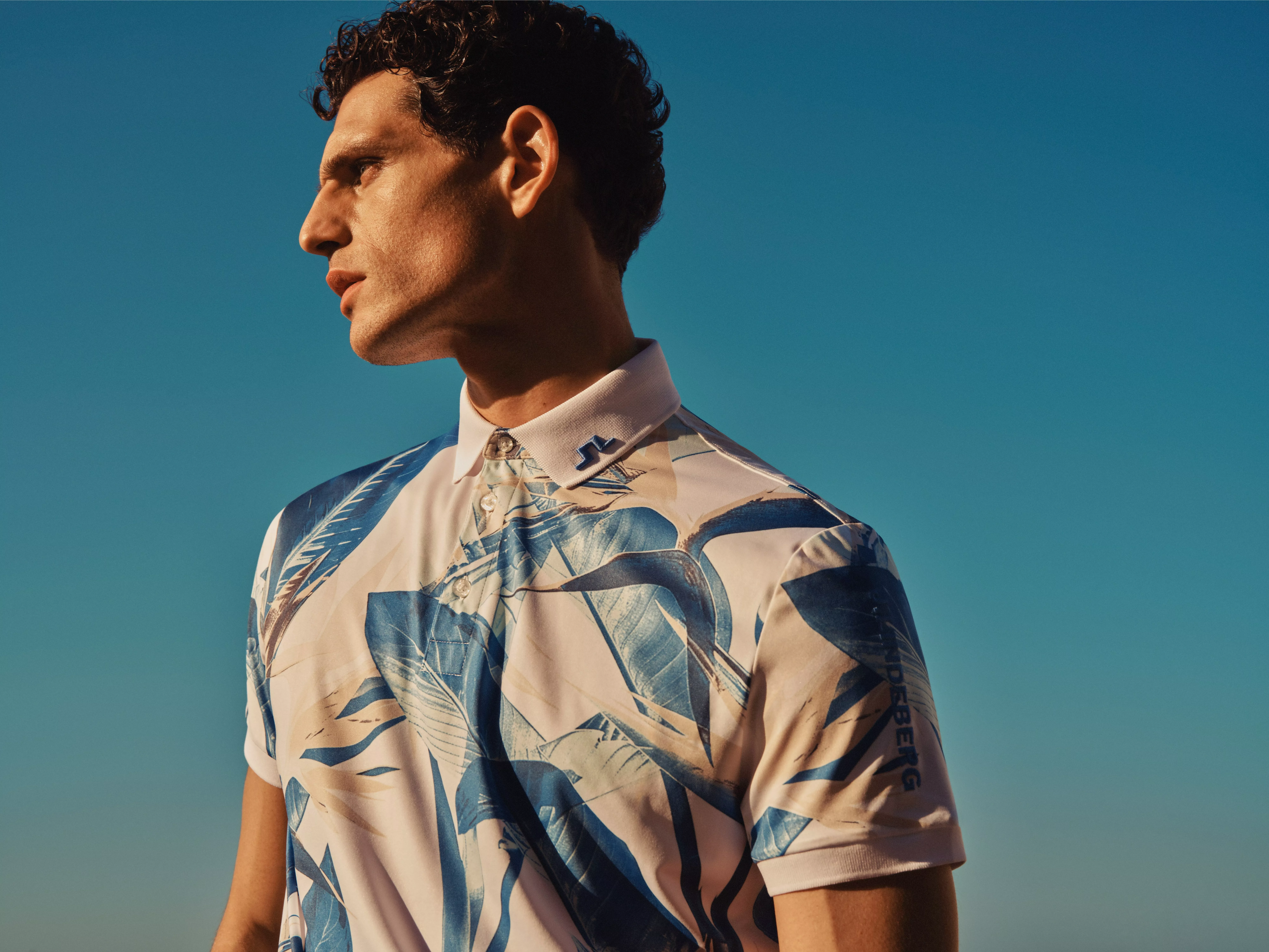 Male model in blue leaf print polo shirt outdoors against clear blue sky