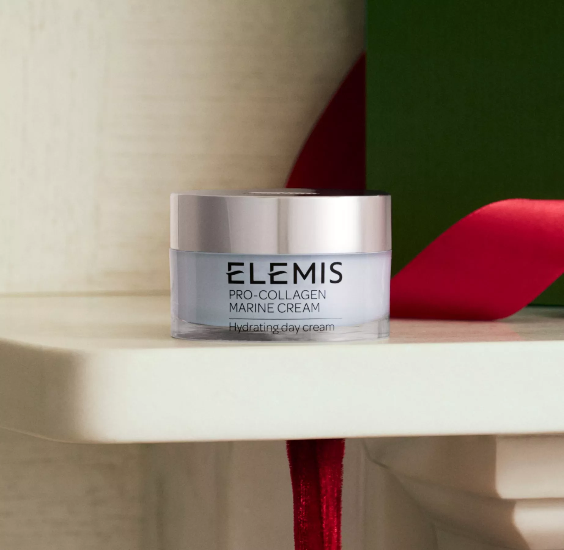 Elemis Pro-Collagen Marine Cream hydrating day moisturiser jar on shelf with red ribbon and green backdrop