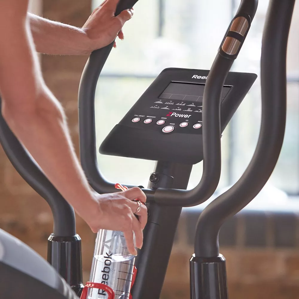 Man using NordicTrack VU 29 upright exercise bike at home, indoor cardio workout with console and water bottle.