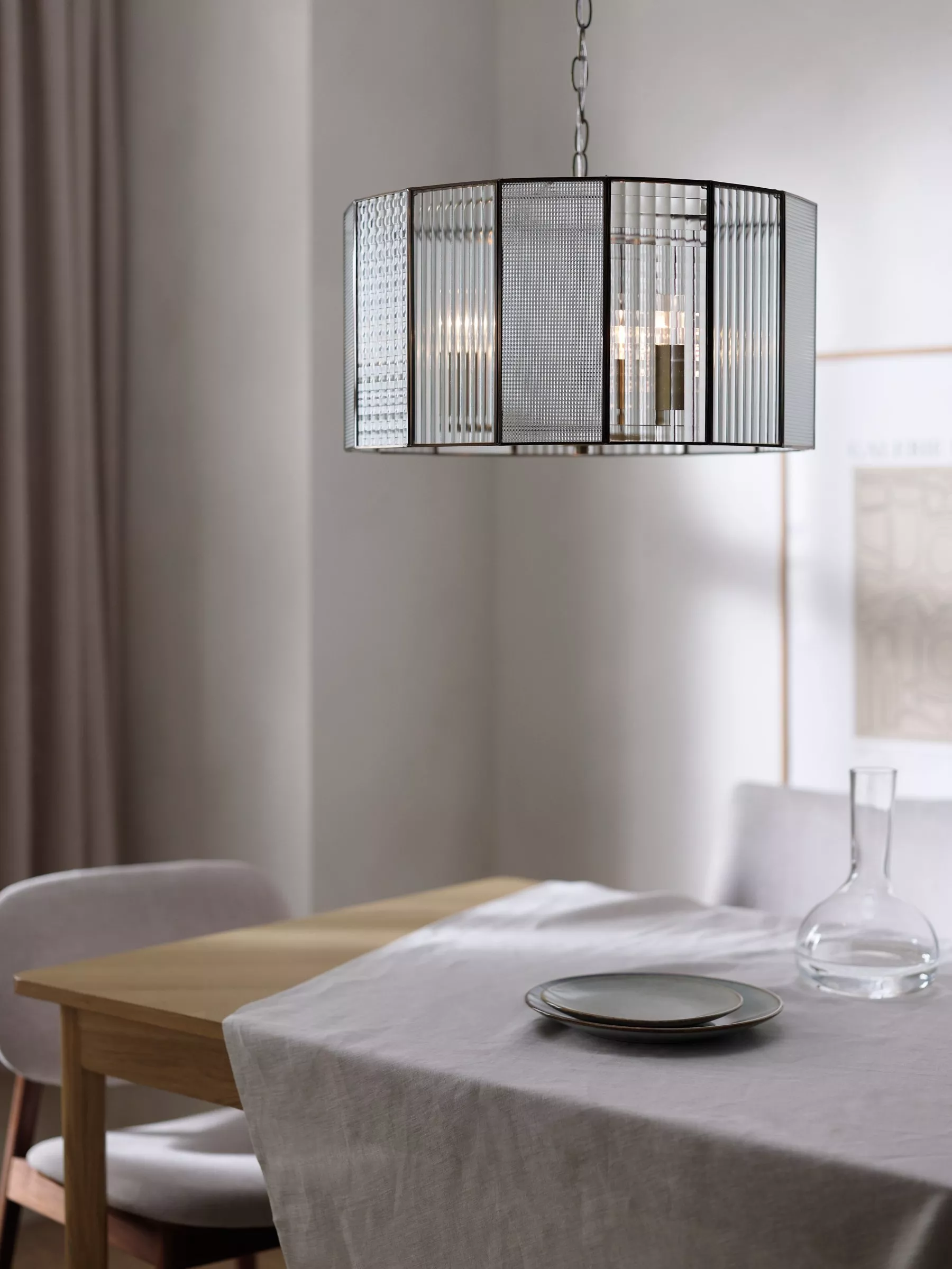 Modern glass and metal pendant ceiling light above minimalist dining table with linen cloth and plates.