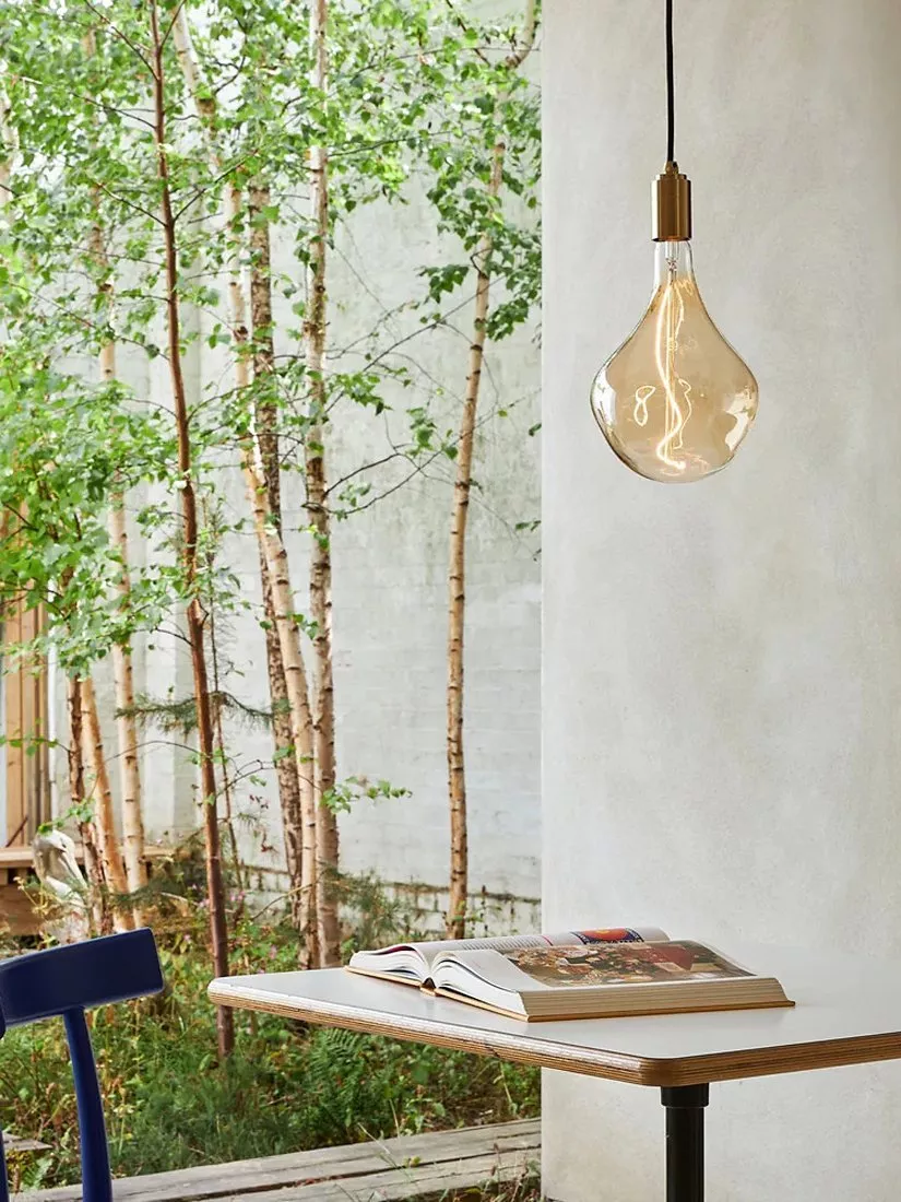 Three hanging vintage Edison filament bulbs with brass holders on black cords against a white wall background