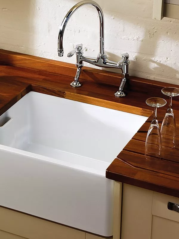 White Belfast kitchen sink with chrome bridge mixer tap set in wooden worktop, with upside-down wine glasses nearby
