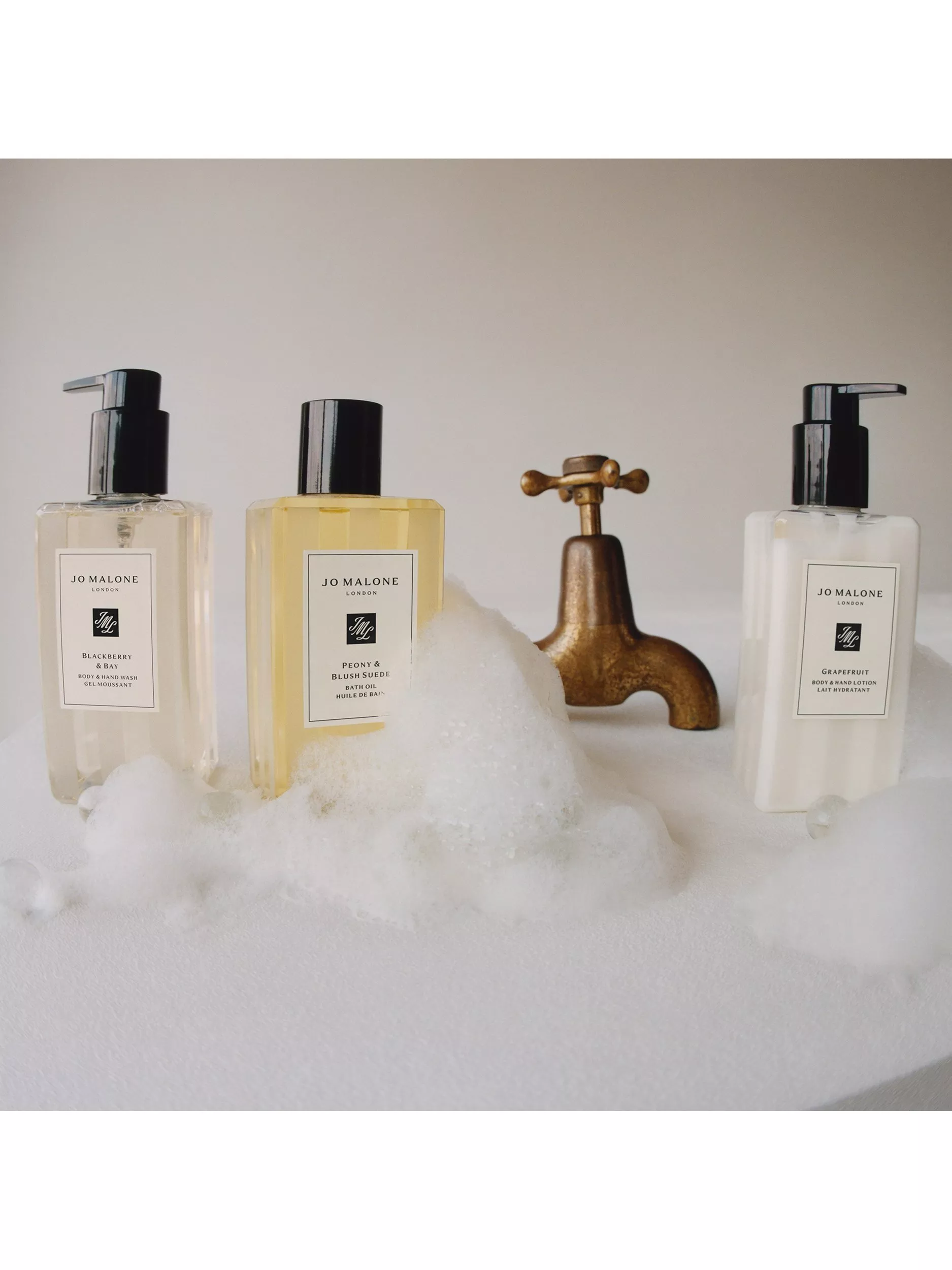 Jo Malone bath and body products in foamy bubbles beside vintage brass tap, luxury bathroom skincare display
