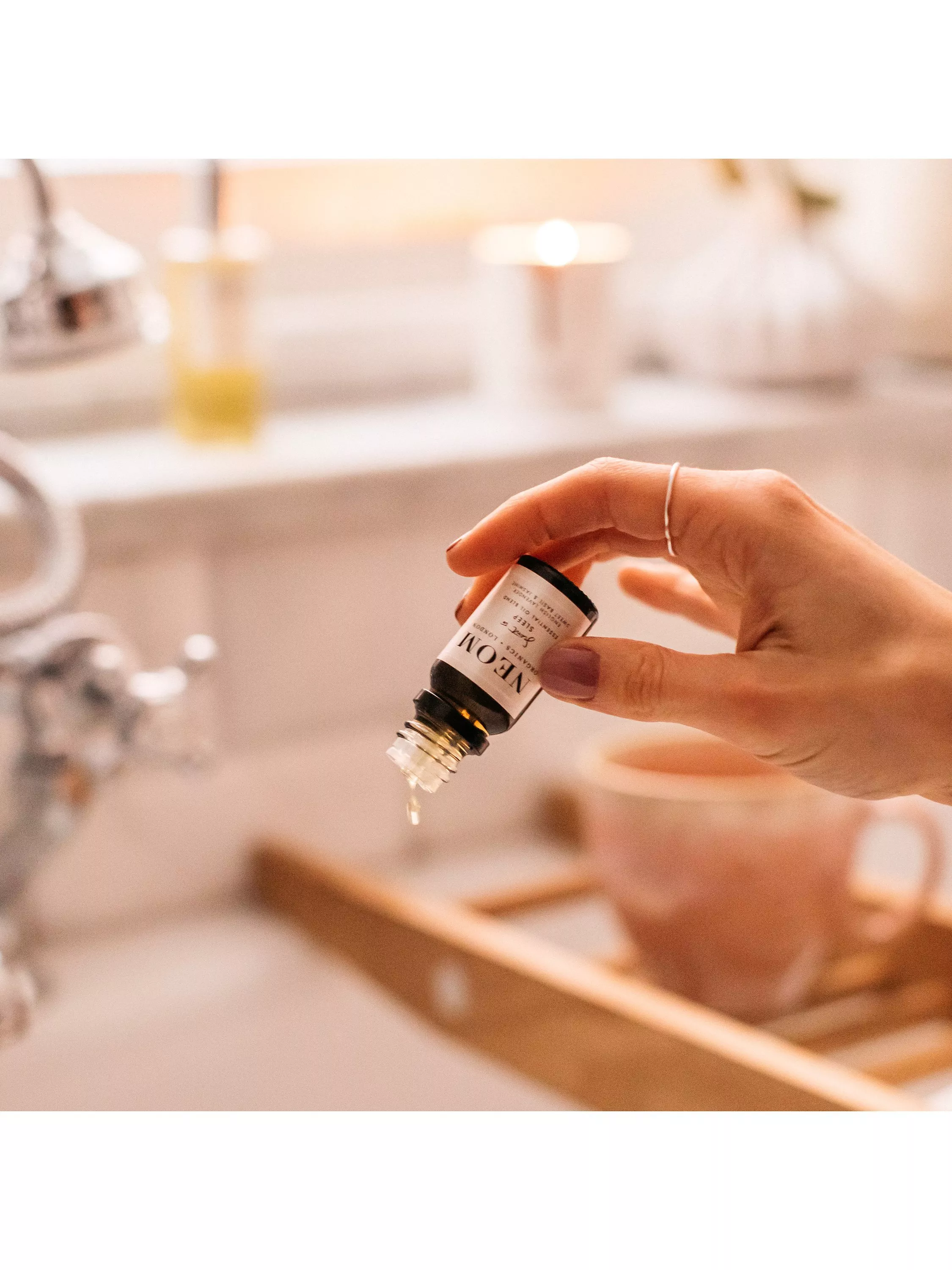 woman adding neom essential oils to a bath 