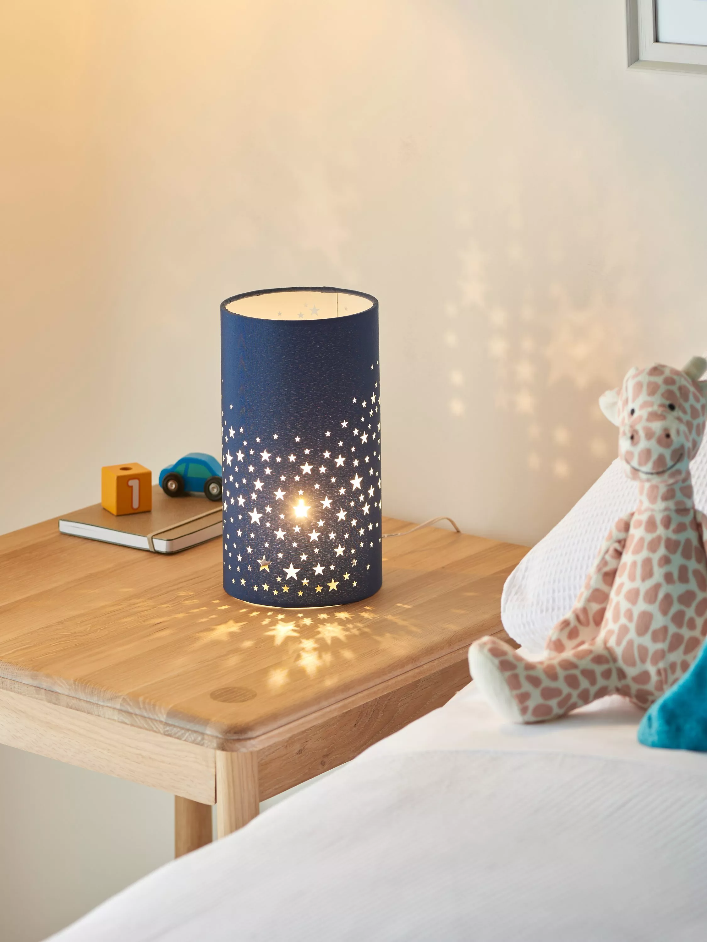 Star projector night light on wooden bedside table in child’s bedroom, casting star patterns on the wall