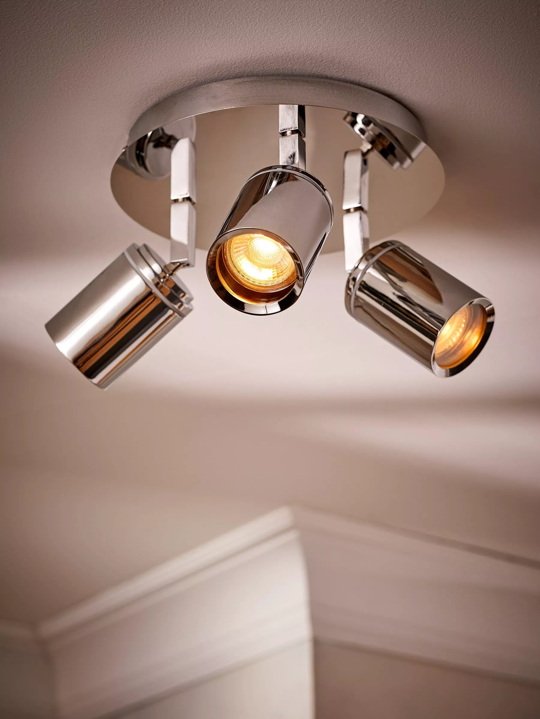 Modern chrome ceiling spotlight bar with three adjustable heads, warm bulbs, mounted on a white ceiling