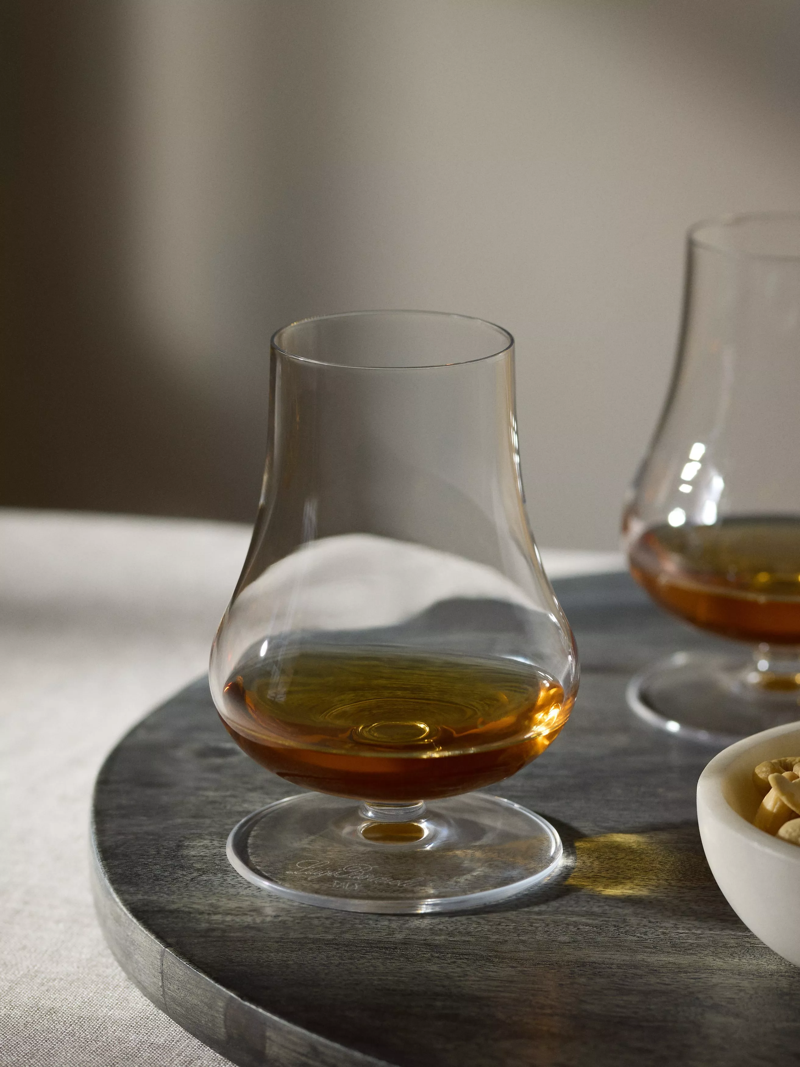 Glencairn whisky tasting glass with amber Scotch on a slate board, soft light and snack bowl nearby