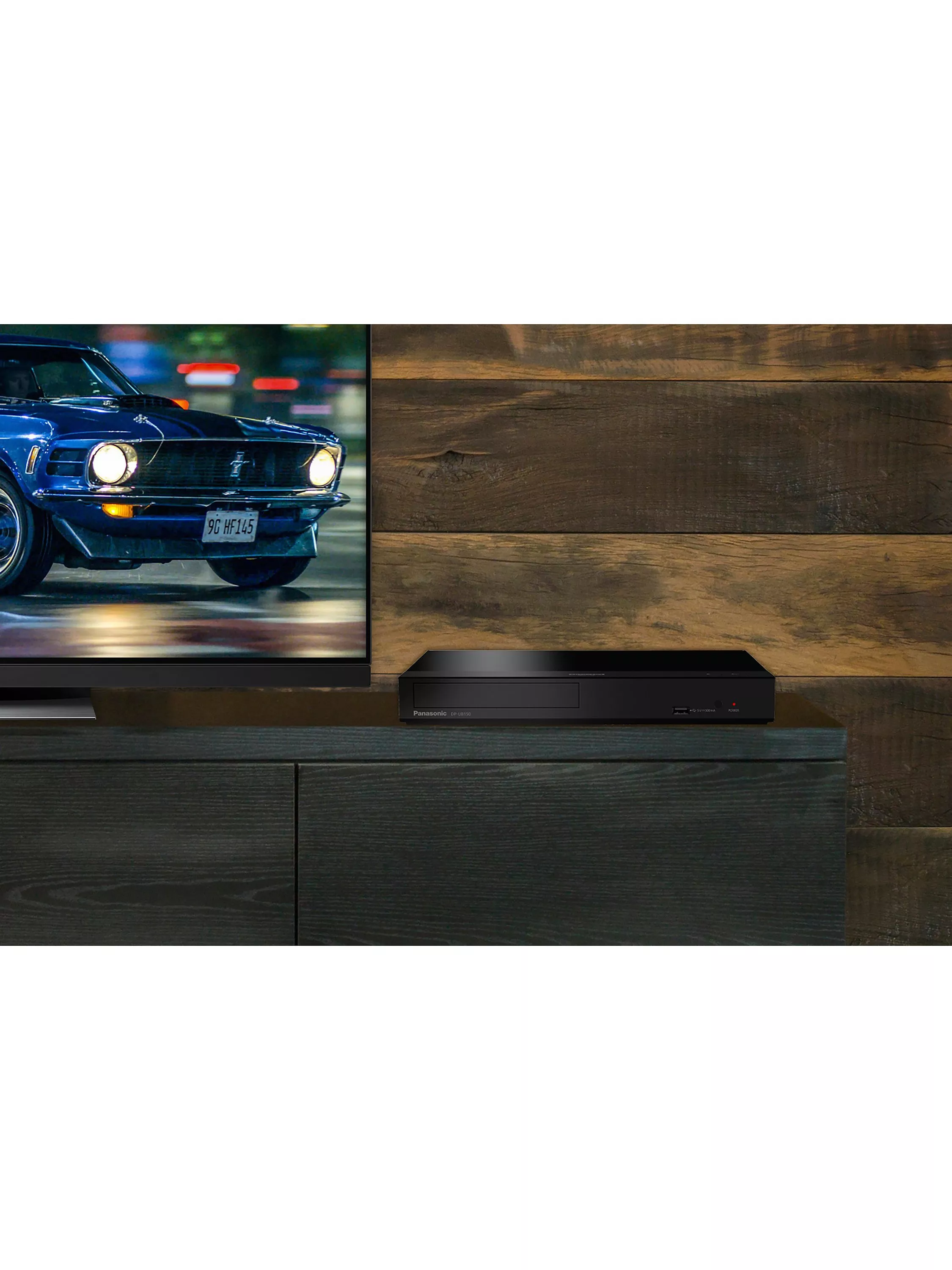 A sleek black Blu-ray player on a dark wooden TV stand next to a television displaying a classic car.