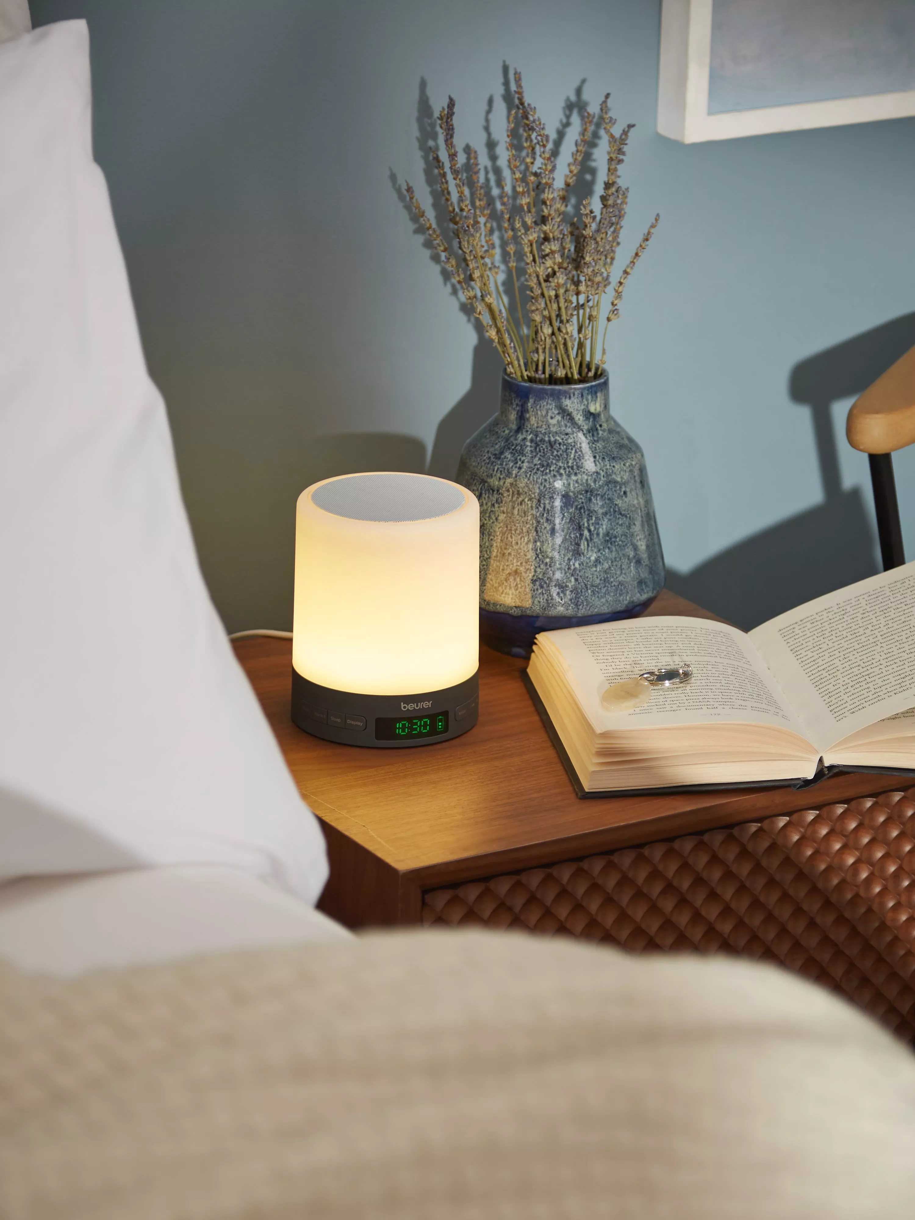 SAD lamp with clock on a bedside table next to a book and vase with lavender in