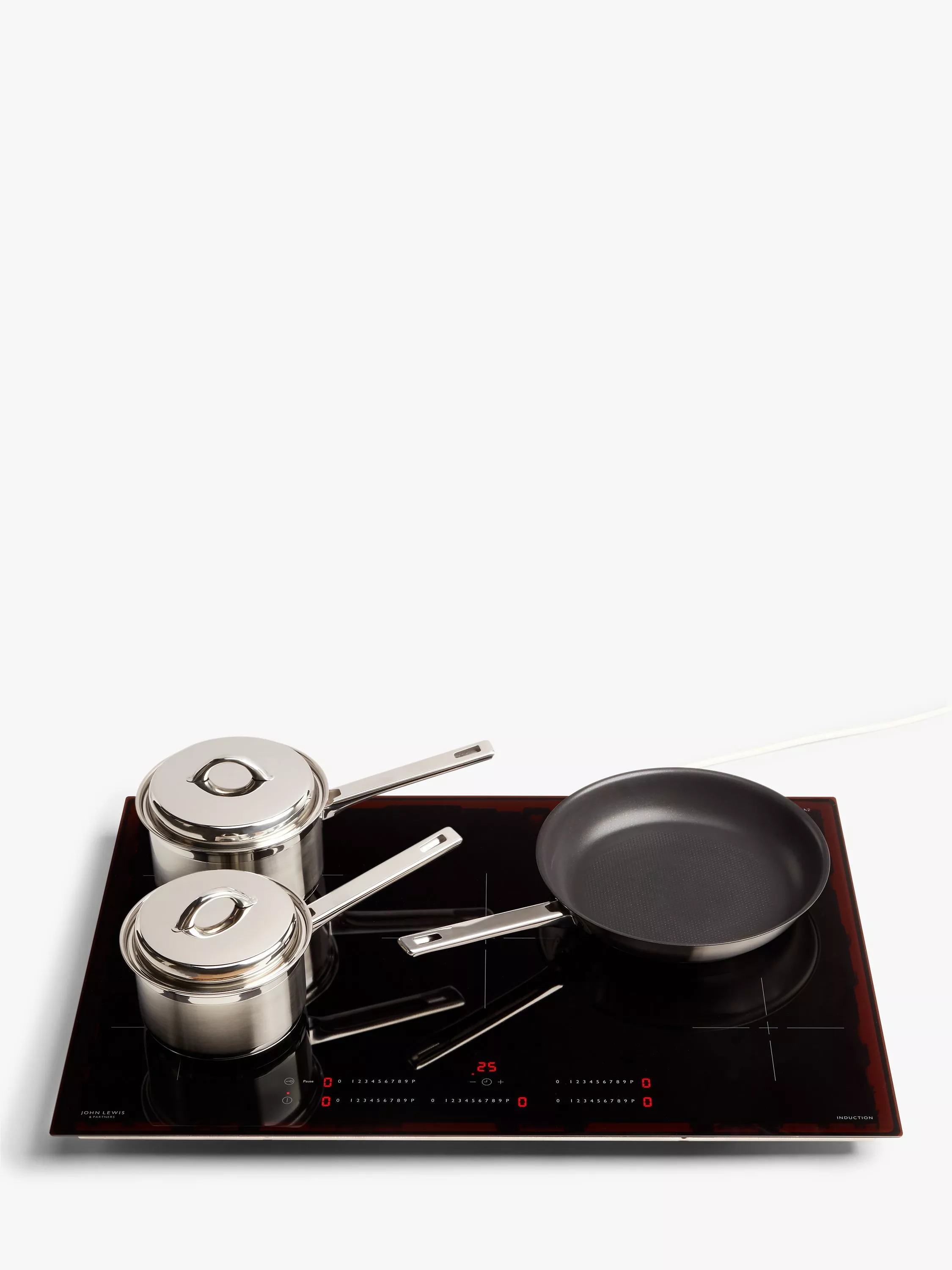 Induction hob with stainless steel saucepans and non-stick frying pan on black glass cooktop, top view
