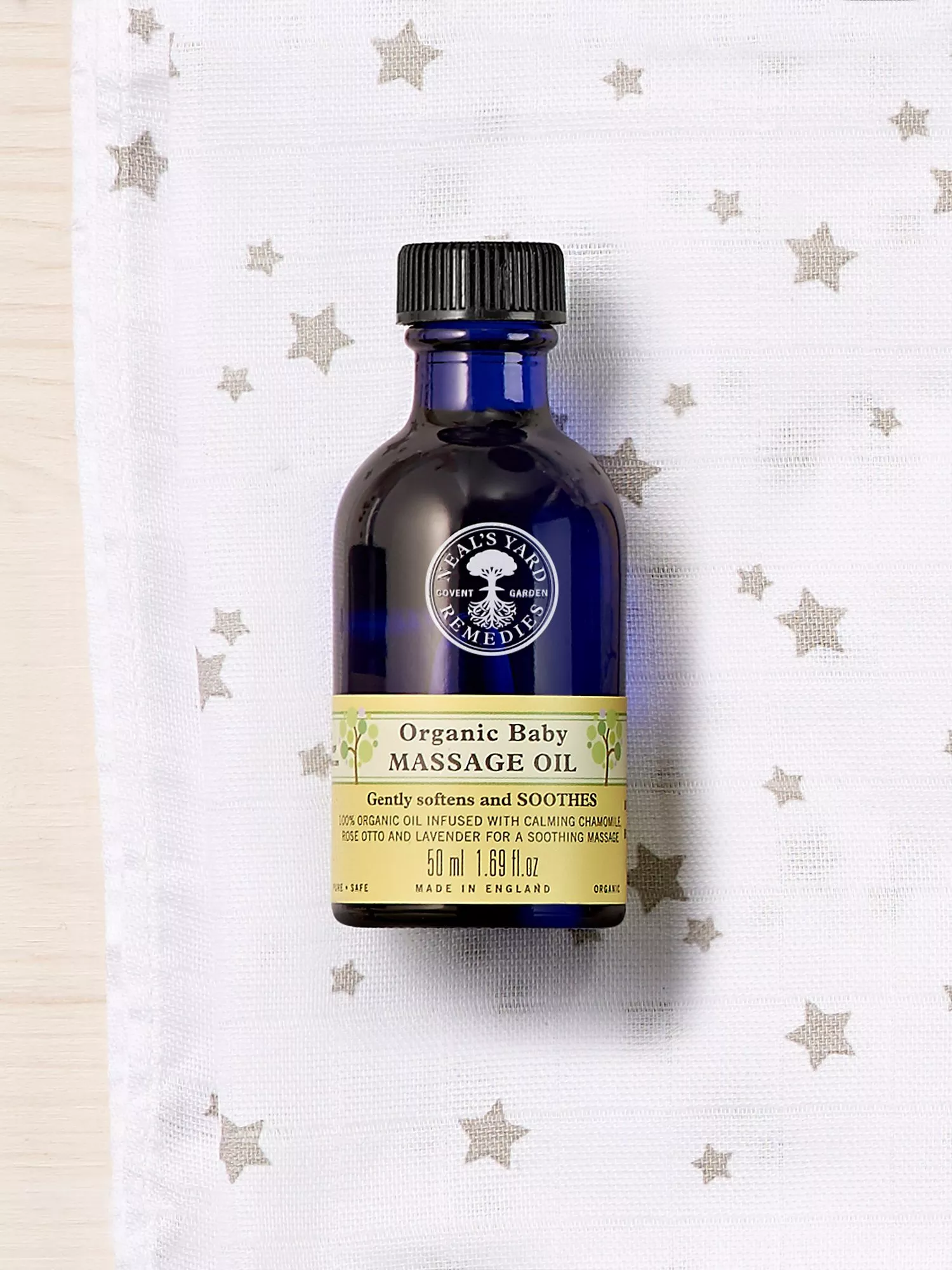 Neal’s Yard Remedies organic baby massage oil bottle on star-pattern muslin cloth, gentle soothing skincare