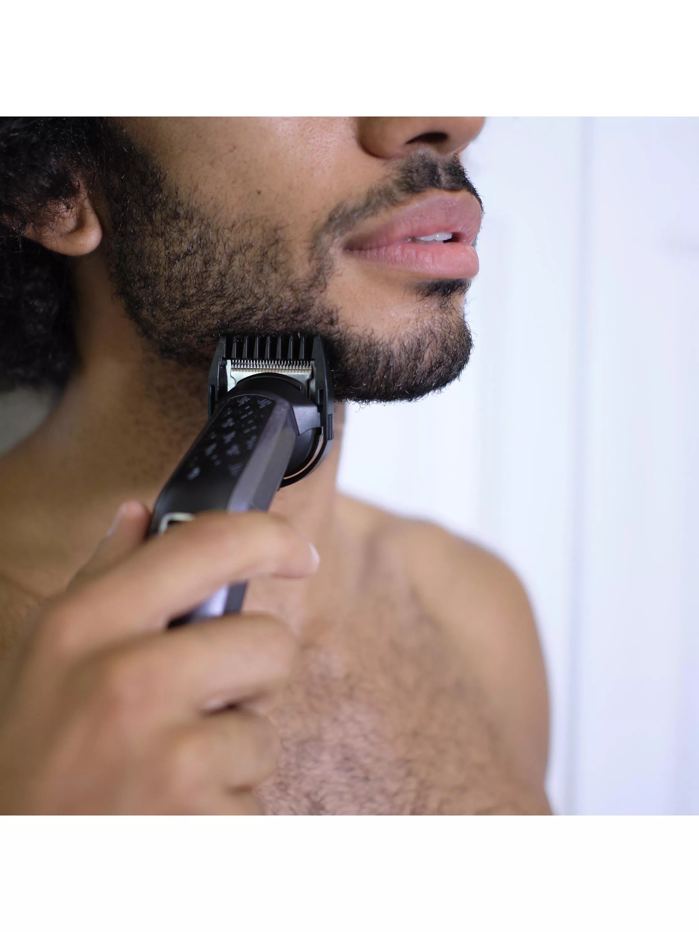 Close-up of man using electric beard trimmer with fading comb attachment for smooth fade grooming at home