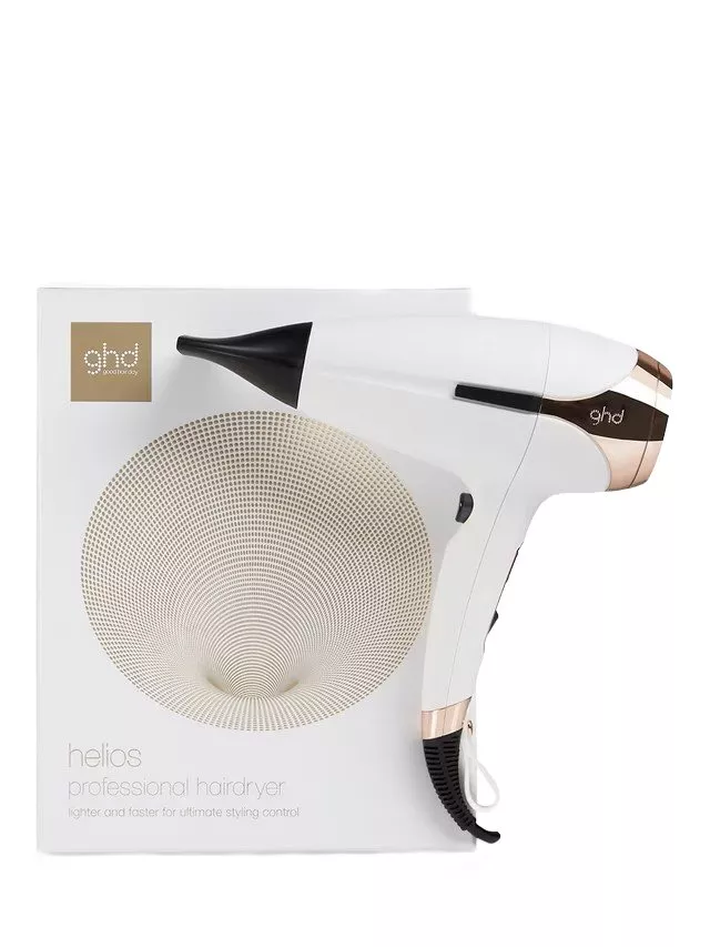 White and gold ghd Helios hairdryer with black nozzle, displayed next to branded packaging box.