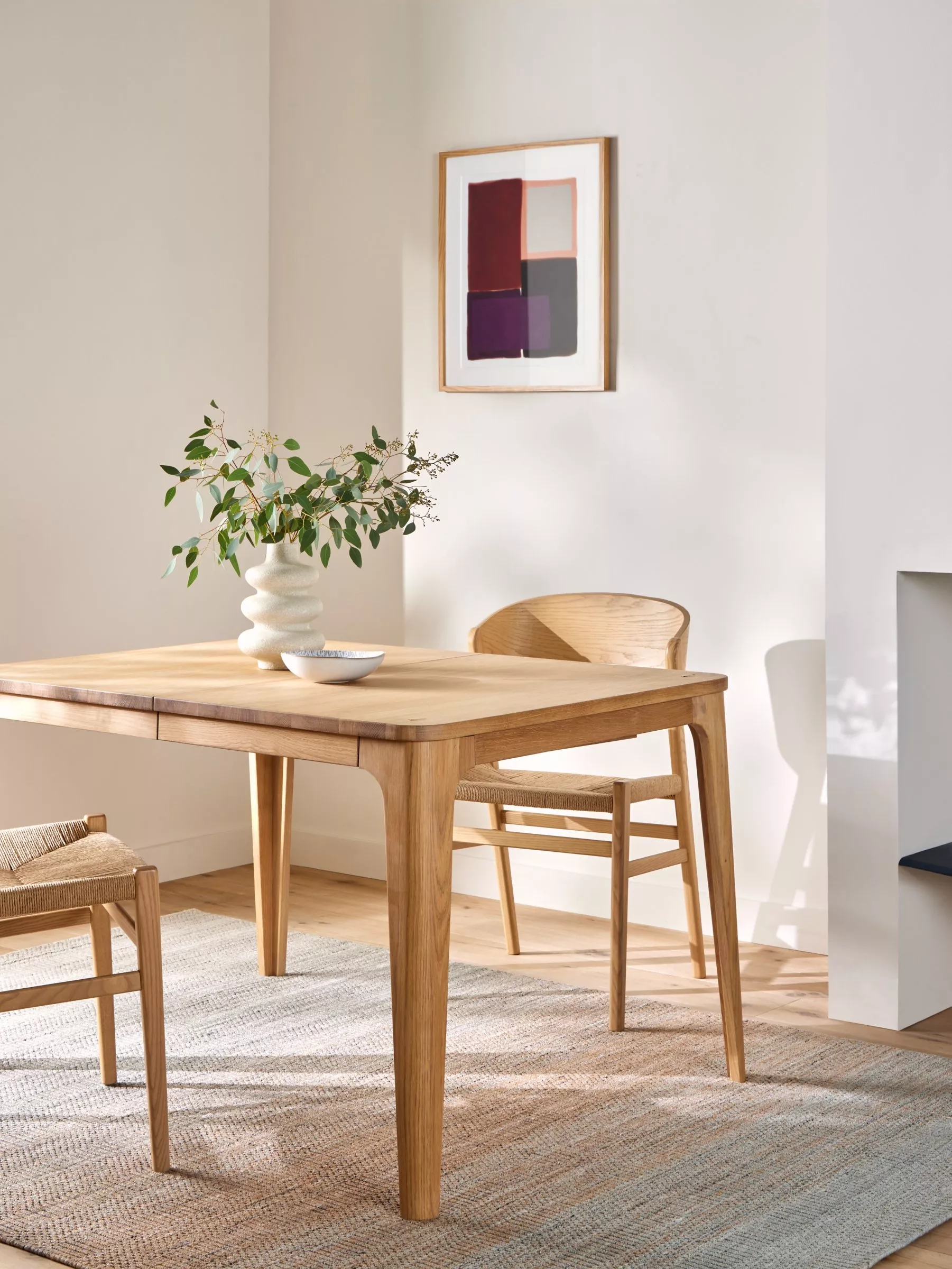 Scandinavian dining room with oak table and chairs, vase of greenery, and framed abstract wall art