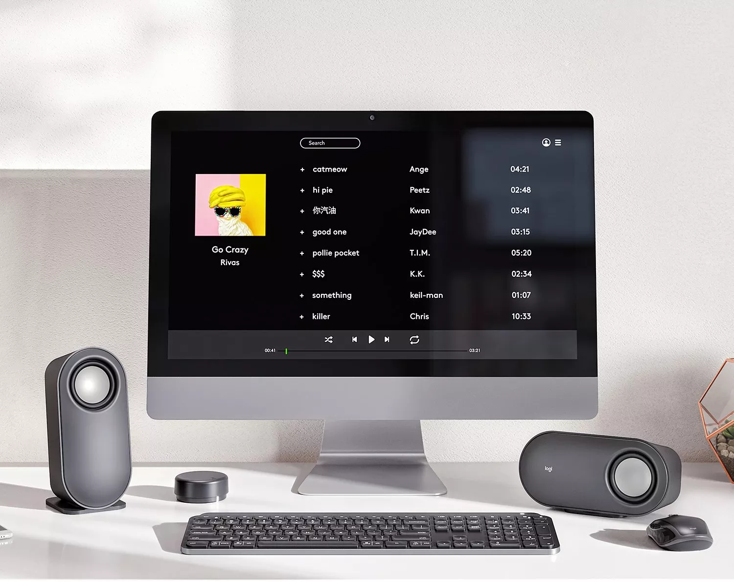 Desktop computer showing music player playlist on screen, with wireless keyboard, mouse and speakers on desk