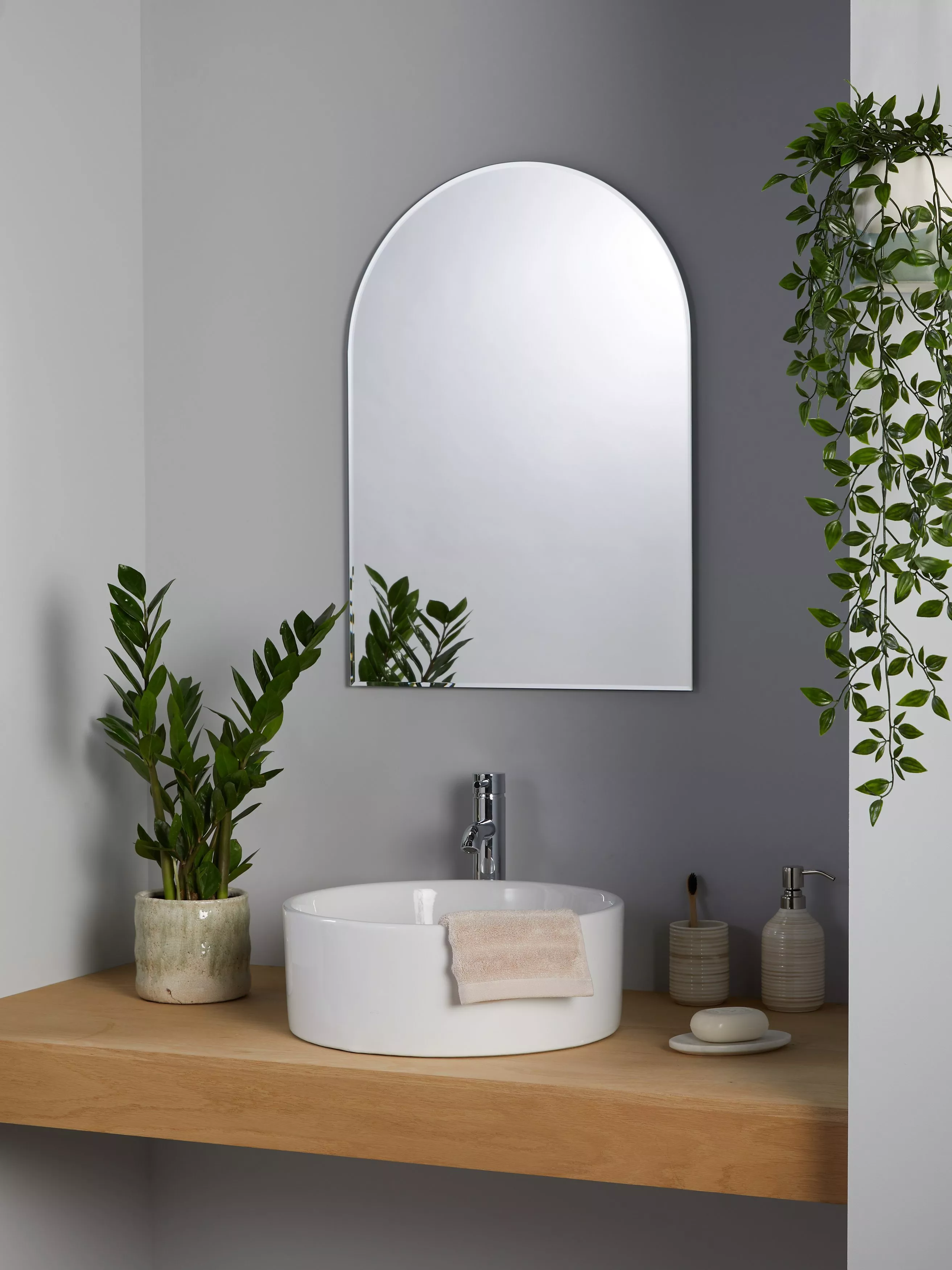 Minimalist bathroom vanity with round white basin, black tap, wall mirror, towels and hanging plant decor