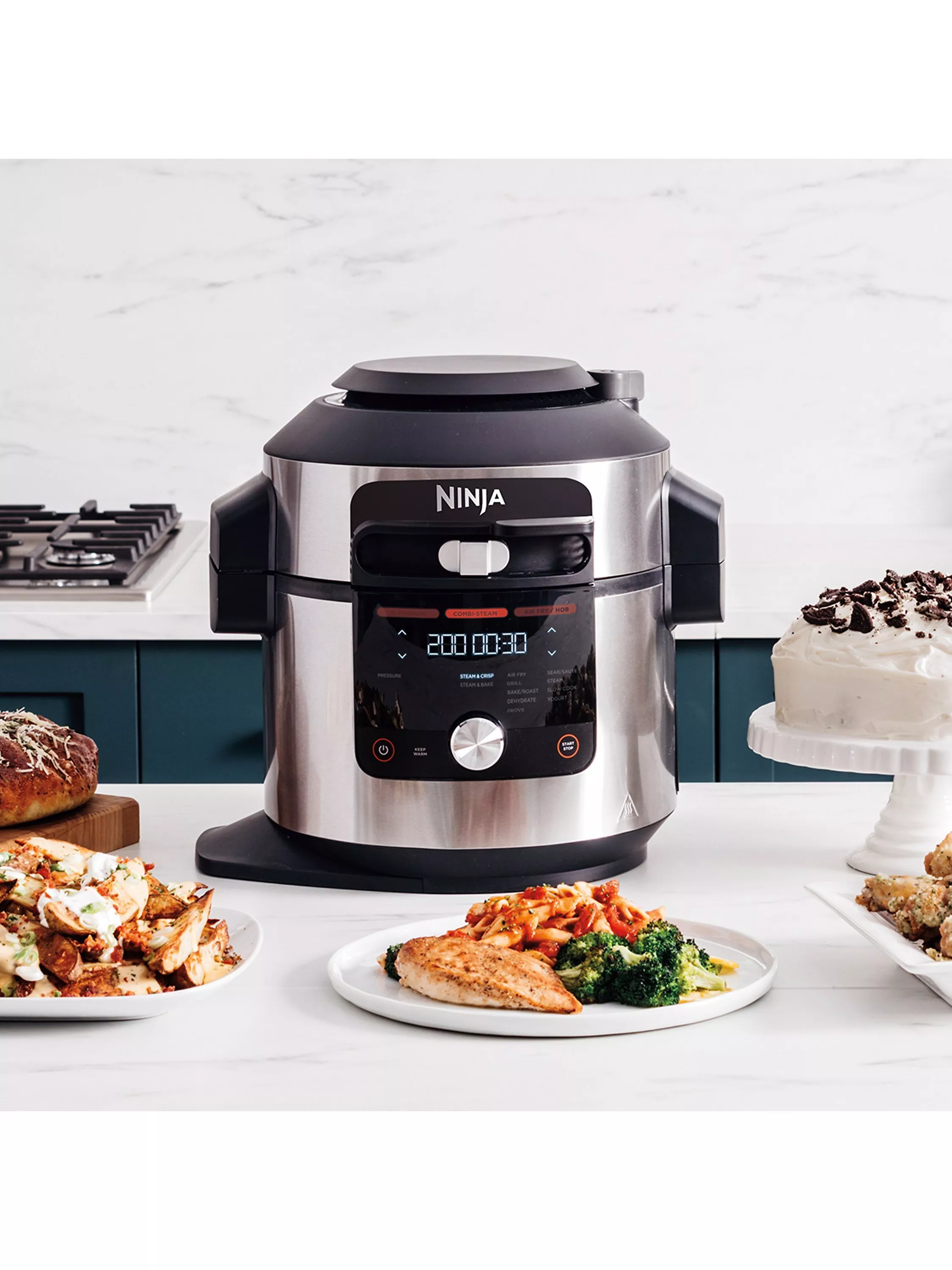 Ninja multi-cooker on modern kitchen worktop with plated meals and dessert, stainless steel pressure cooker appliance