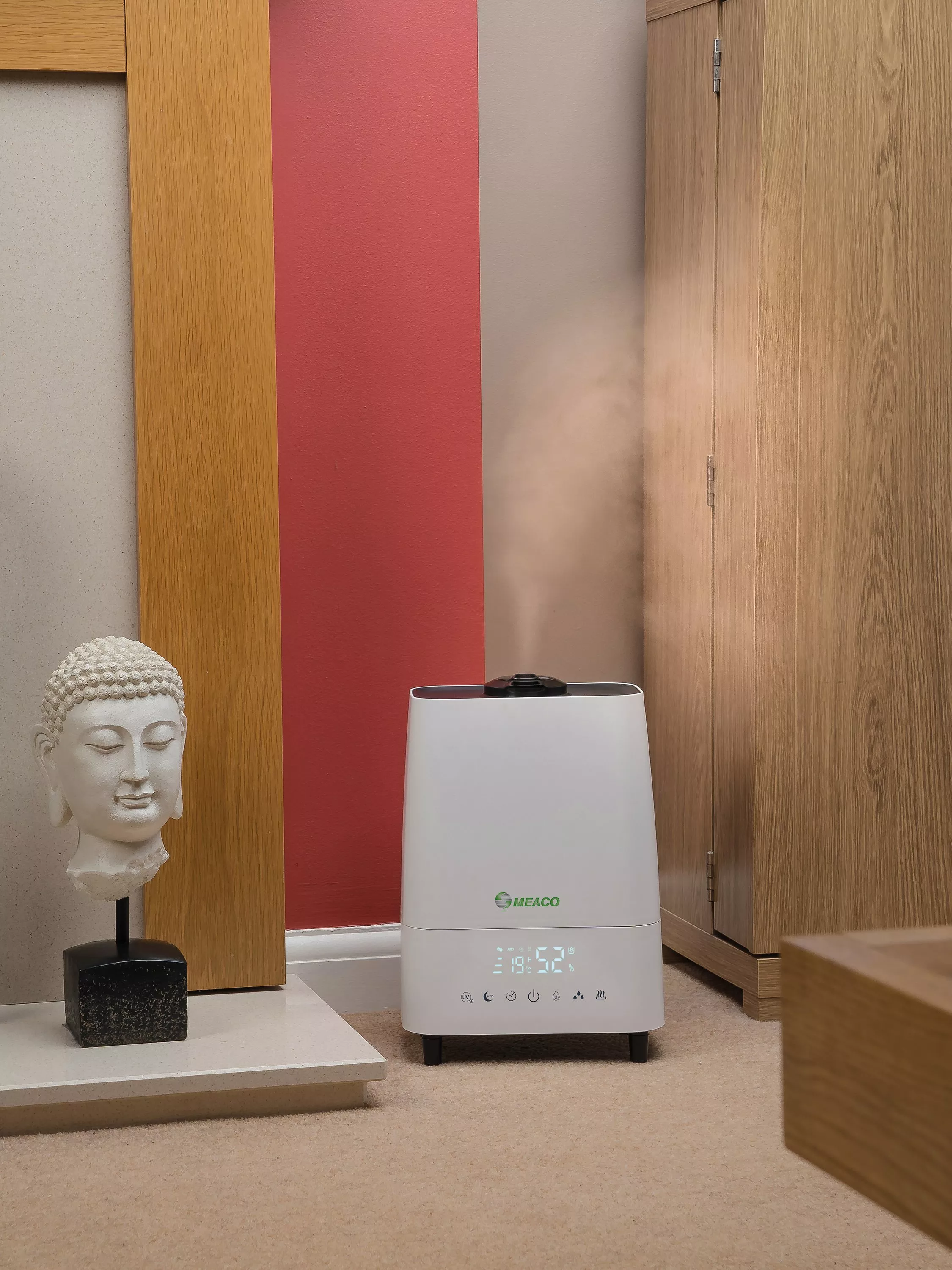 Meaco ultrasonic humidifier releasing mist in modern bedroom corner beside wooden wardrobe and Buddha ornament.