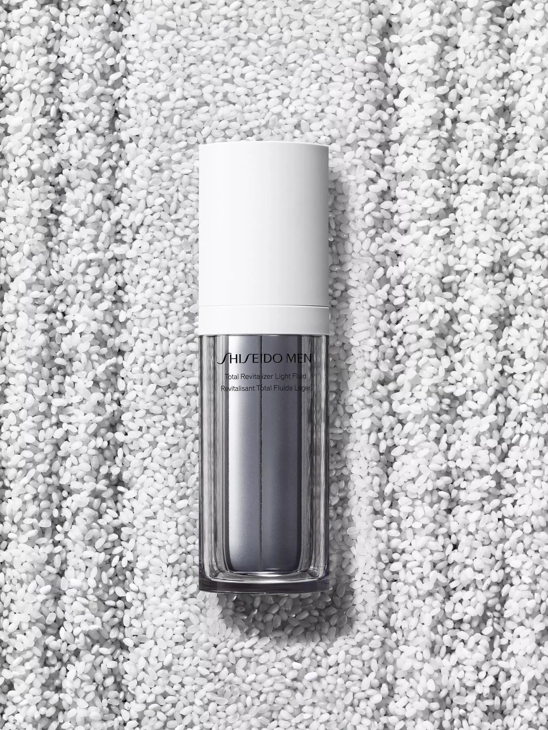 Shiseido Men Total Revitalizer Light Fluid bottle on white rice grains background, premium skincare product shot