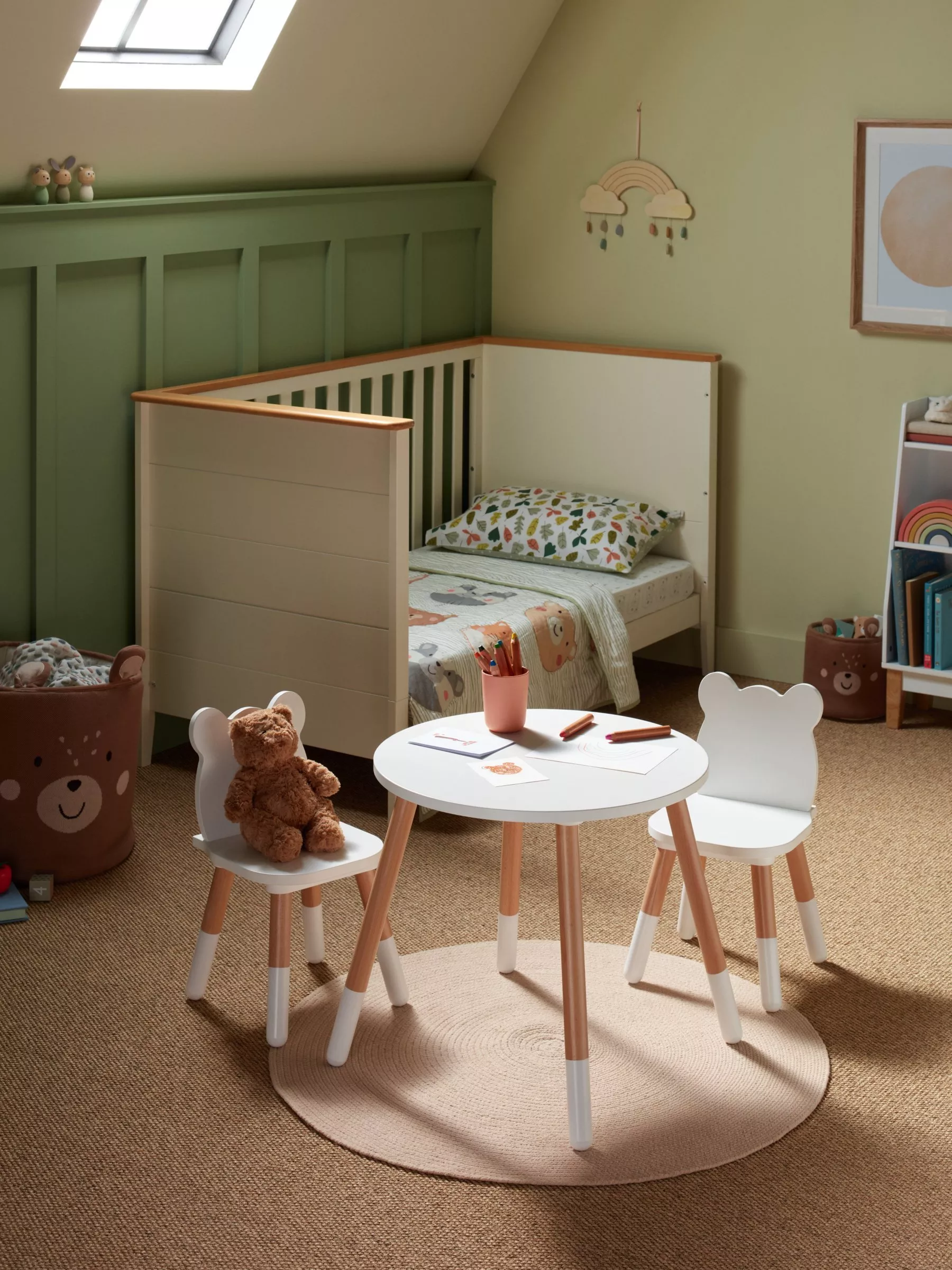Cosy nursery with toddler bed, kids table and chairs, teddy bear, soft green walls and roof skylight.