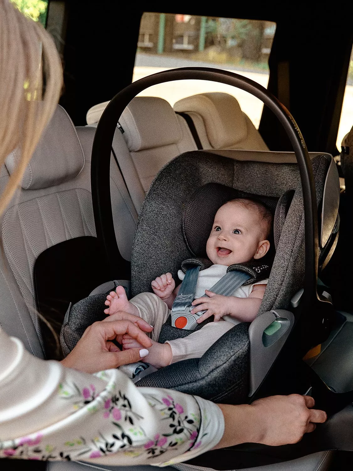 Smiling baby secured in an infant car seat as a parent adjusts straps inside a modern family vehicle interior