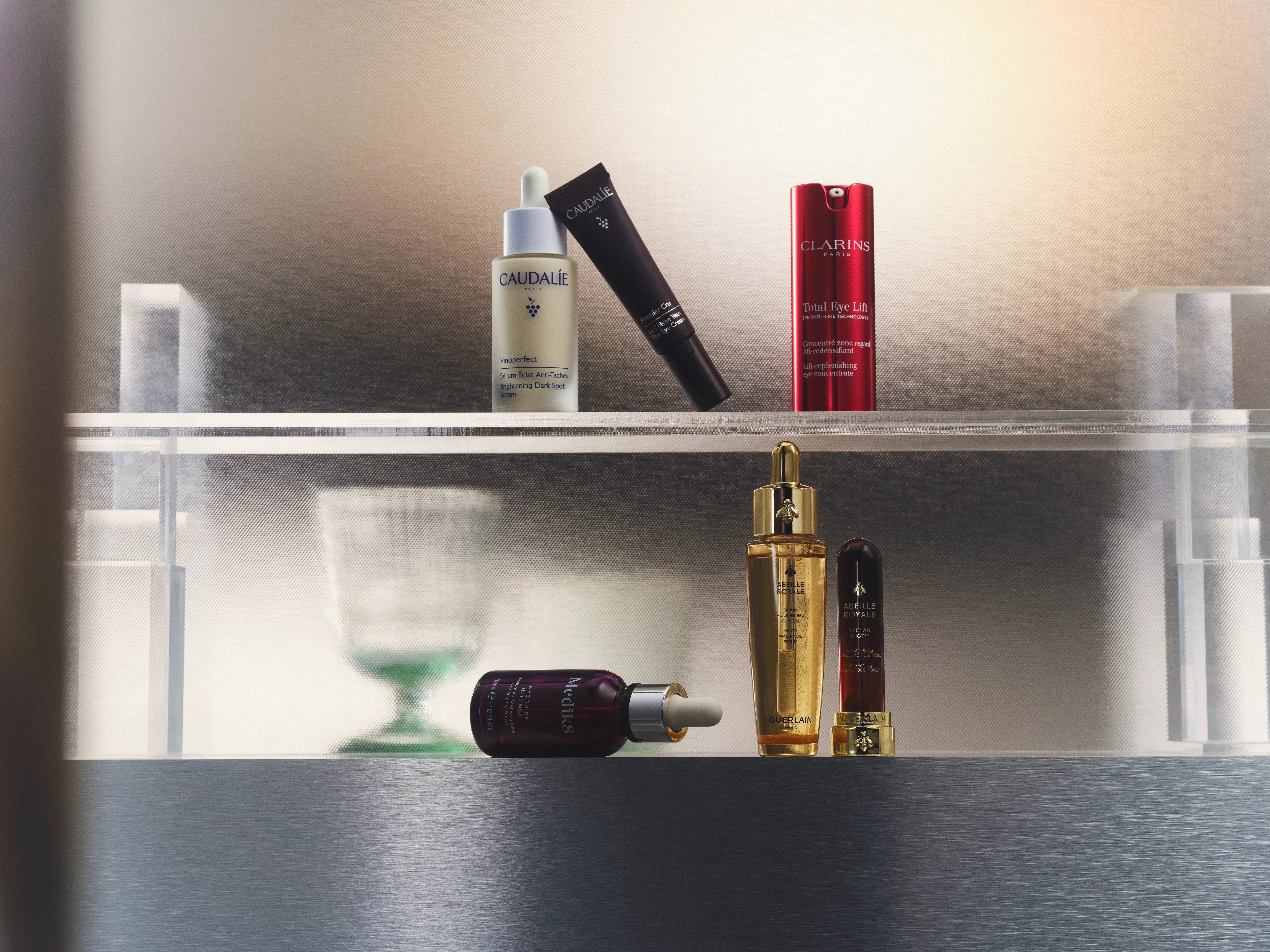 A collection of high-end skincare and beauty products displayed on glass shelves. Visible brands include Caudalie and Clarins, featuring serums and creams in elegant packaging.