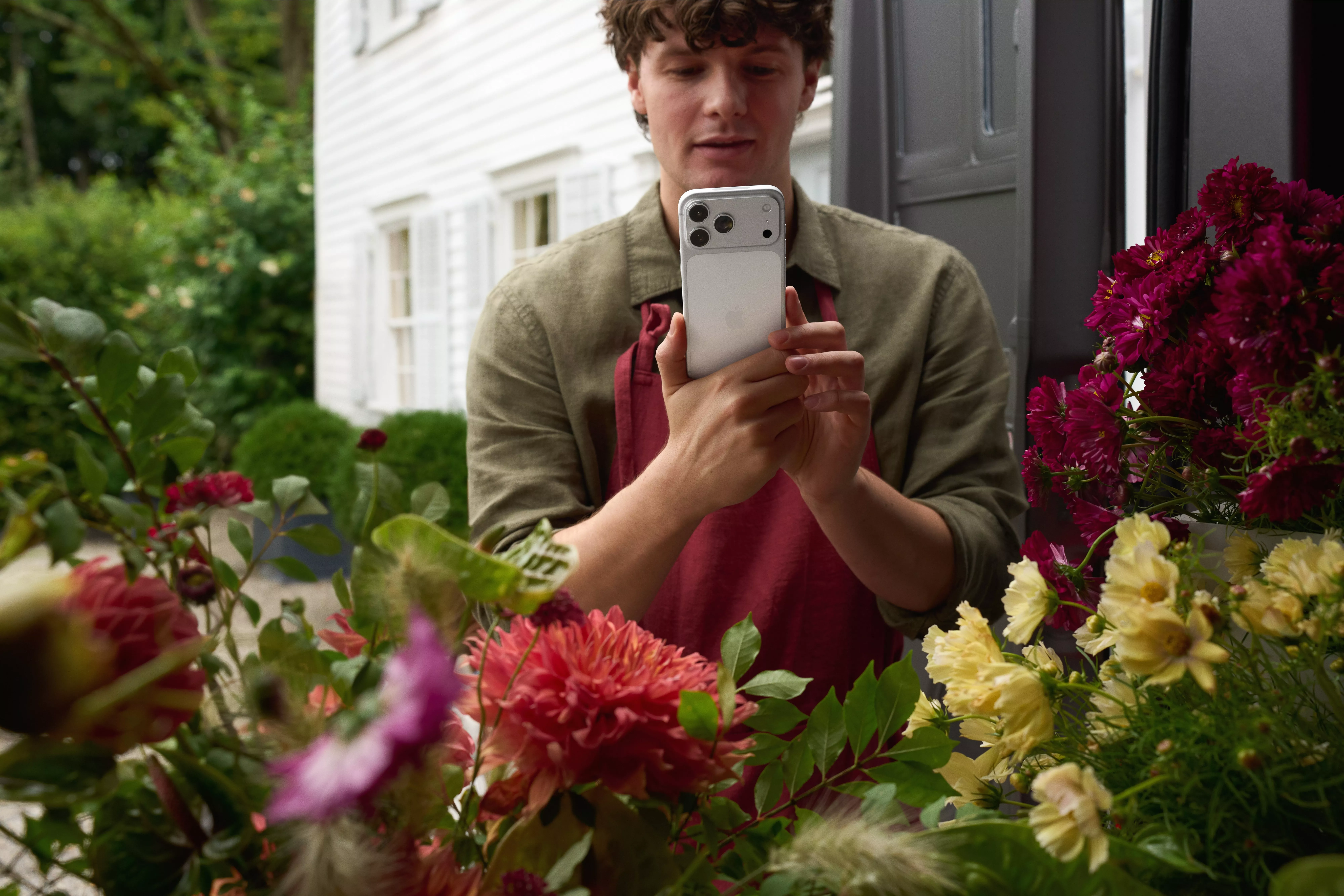 Florist using a smartphone to photograph colourful fresh flowers in a shop doorway for online marketing and sales