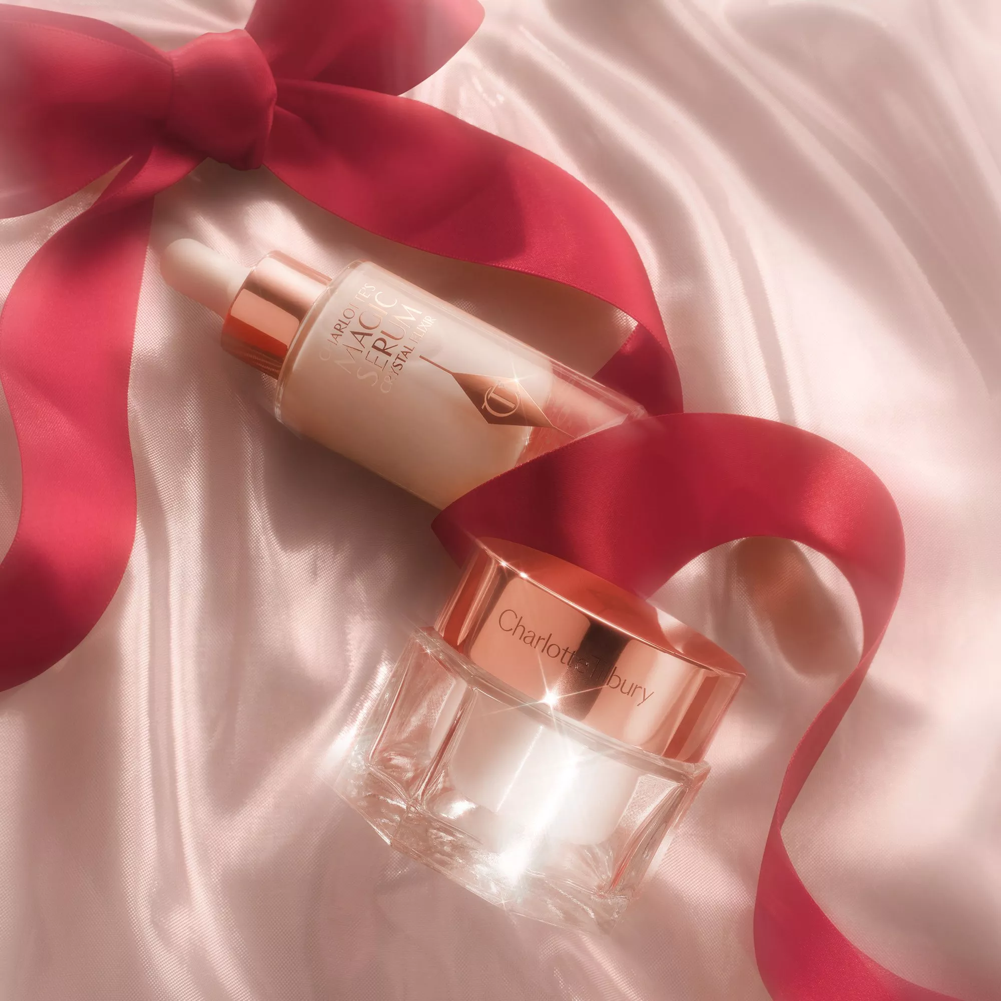 Charlotte Tilbury Magic Serum Crystal Elixir bottle and face cream jar in rose-gold packaging on soft floral backdrop