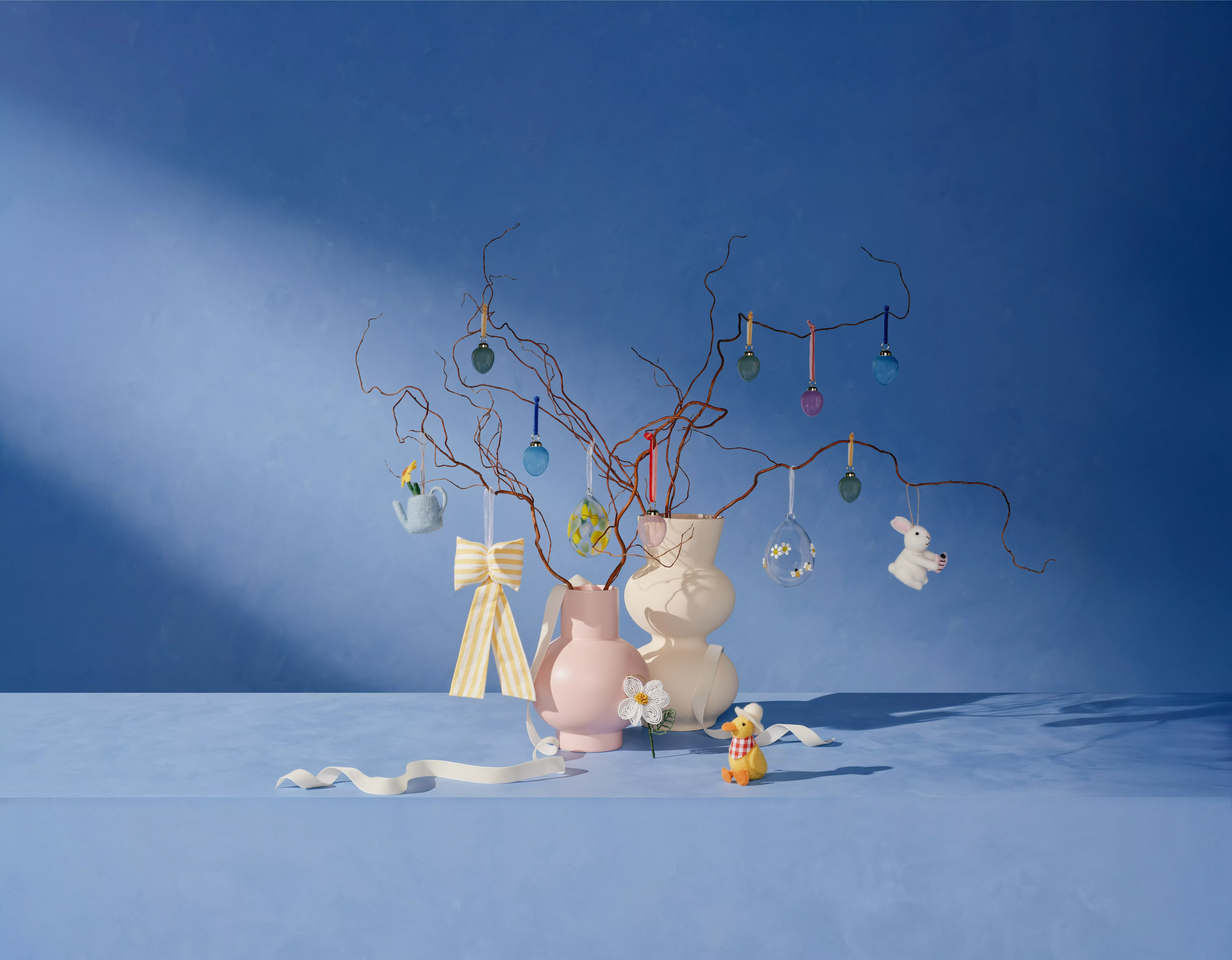 Whimsical Easter arrangement with pastel vases, decorated branches, and festive ornaments against a blue backdrop.