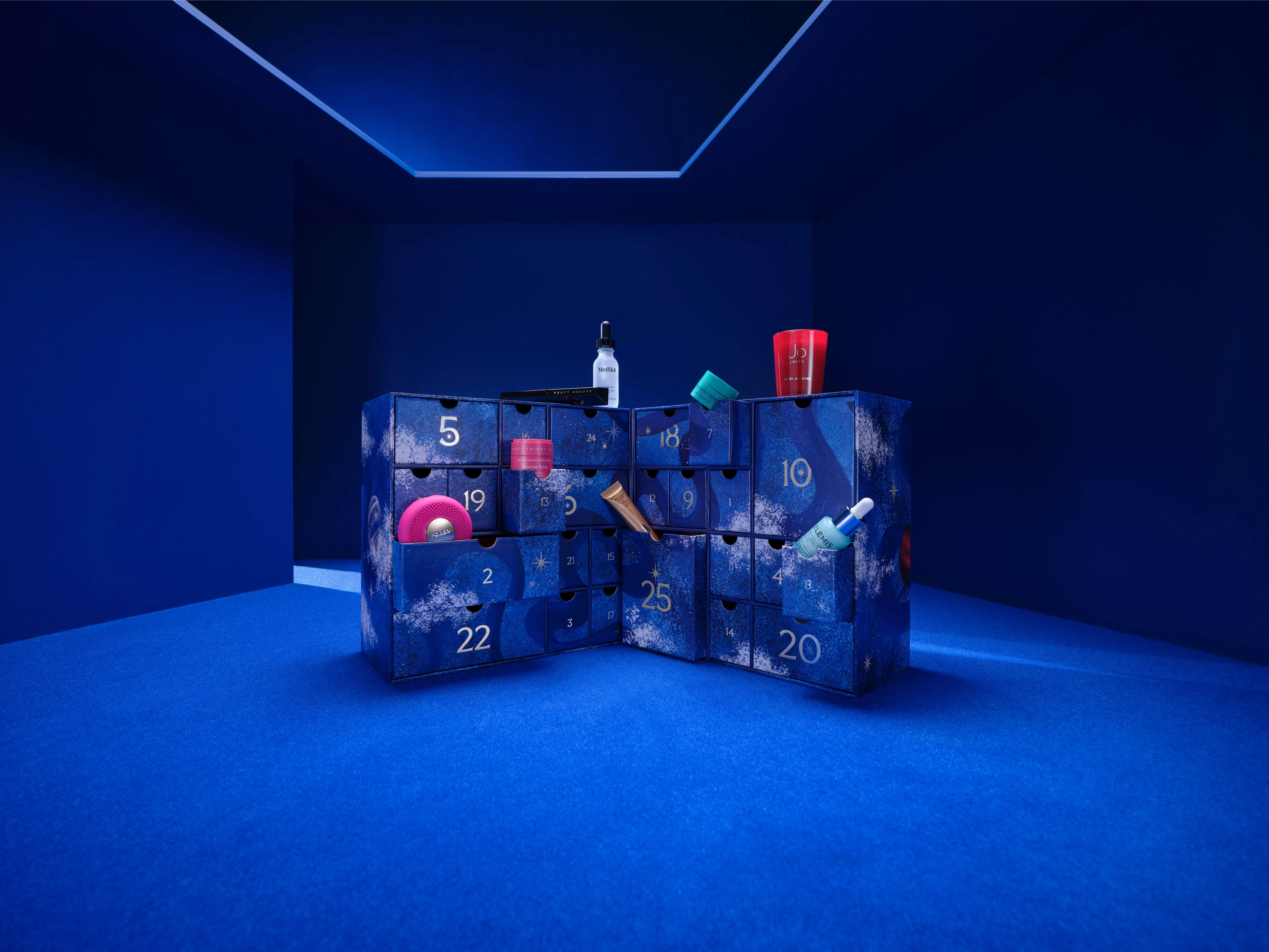 Blue beauty advent calendar with numbered drawers, open compartments showing skincare and cosmetic products in studio set