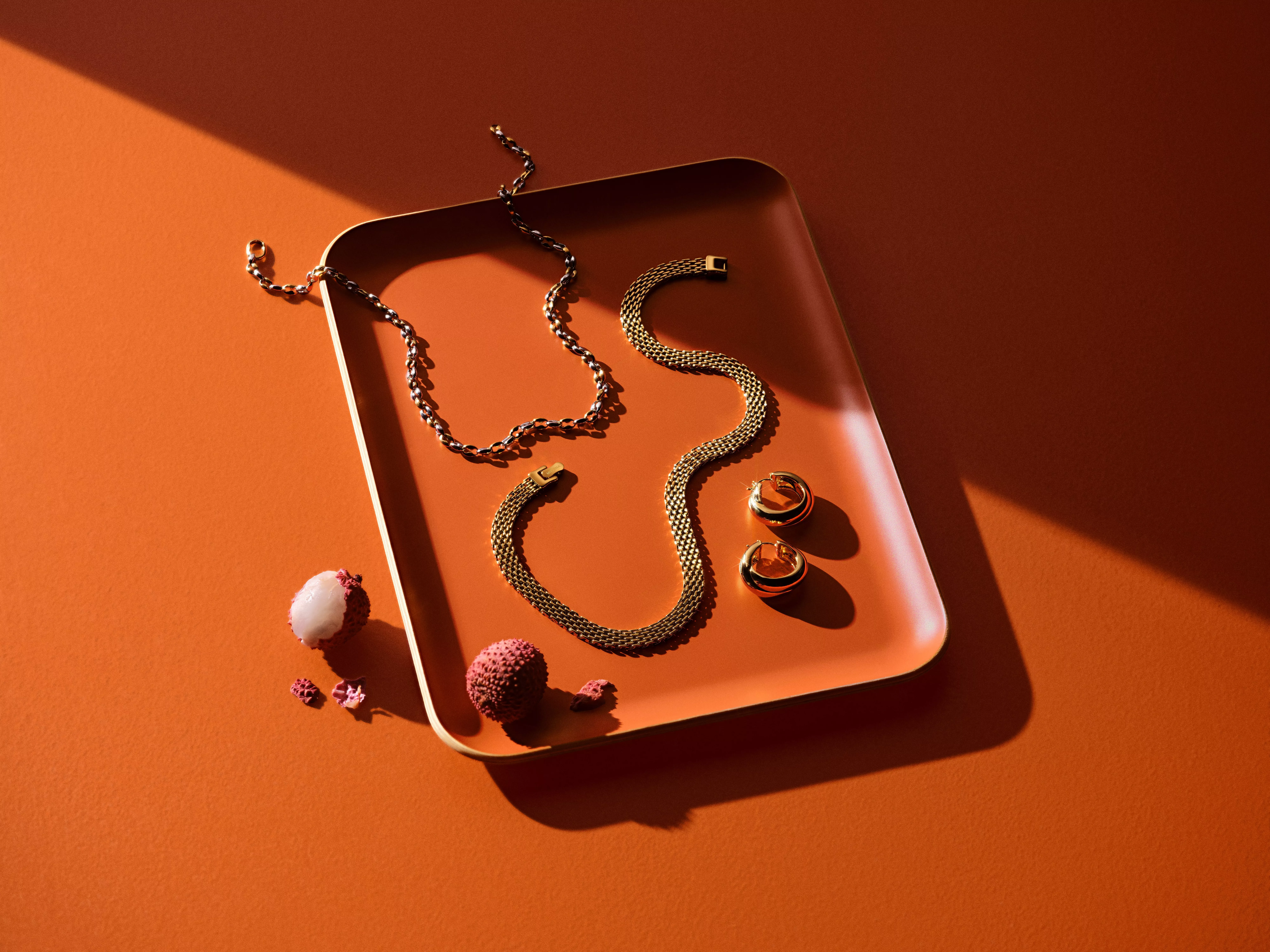 Gold chain necklace, chunky bracelet and hoop earrings on tray, warm terracotta background flat lay photo