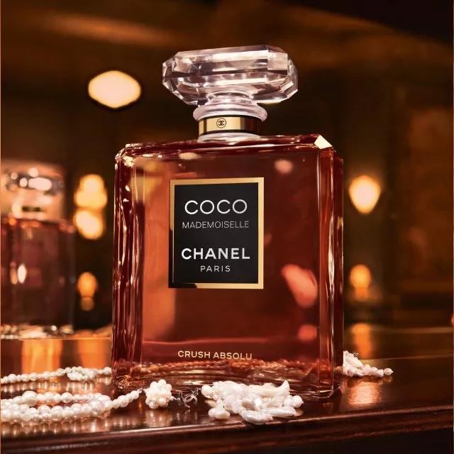 Chanel Coco Mademoiselle perfume bottle on glossy table with pearl necklace and warm bokeh lighting background