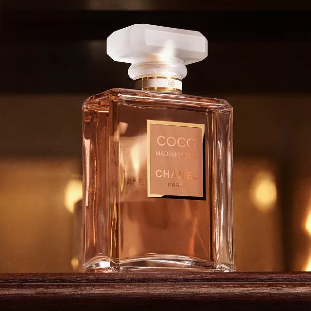 Close-up of Chanel Coco Mademoiselle perfume bottle on wooden surface with warm golden background lighting