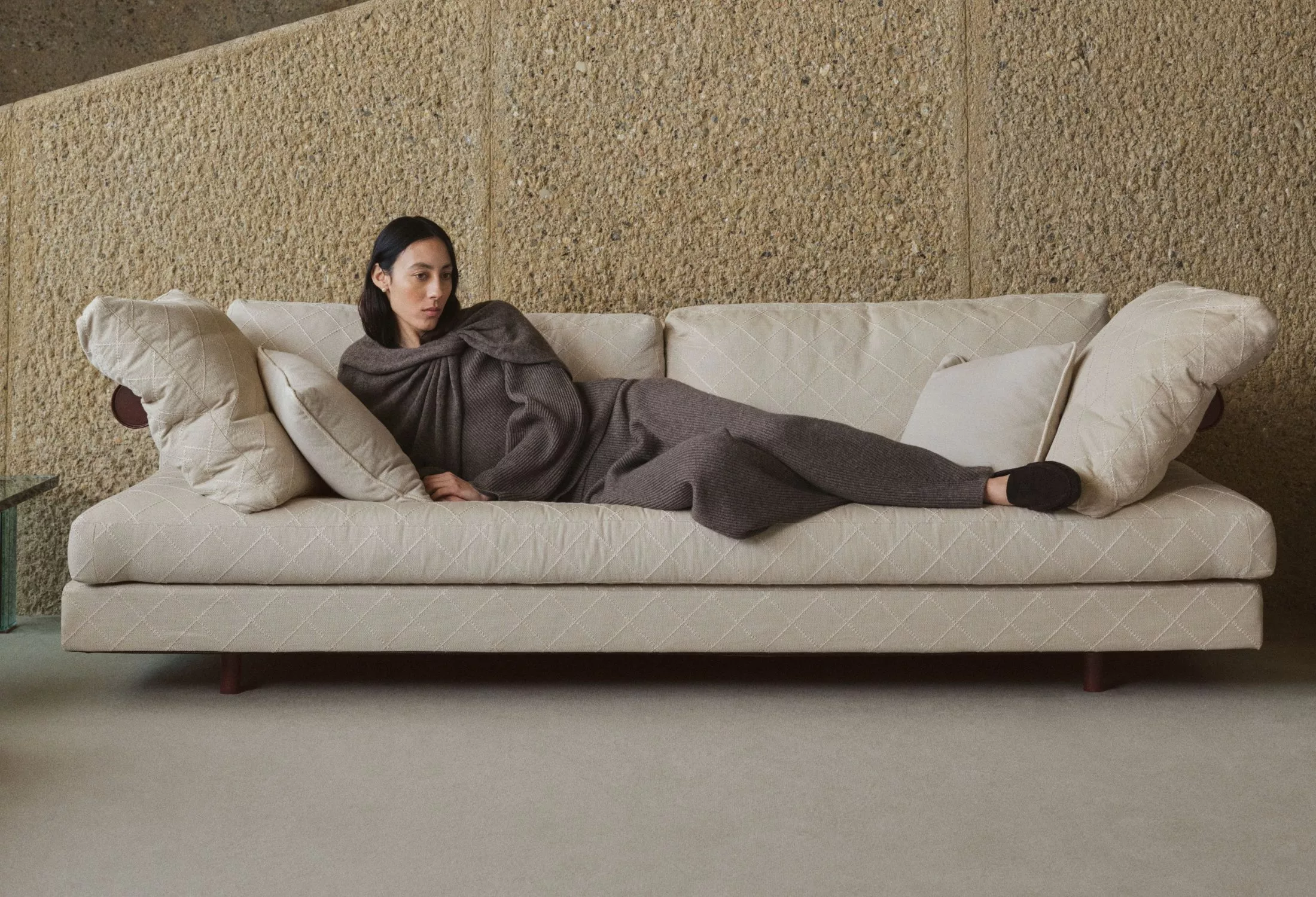 Woman reclining on a cream quilted sofa in a minimalist living room, wearing a cosy knit loungewear set