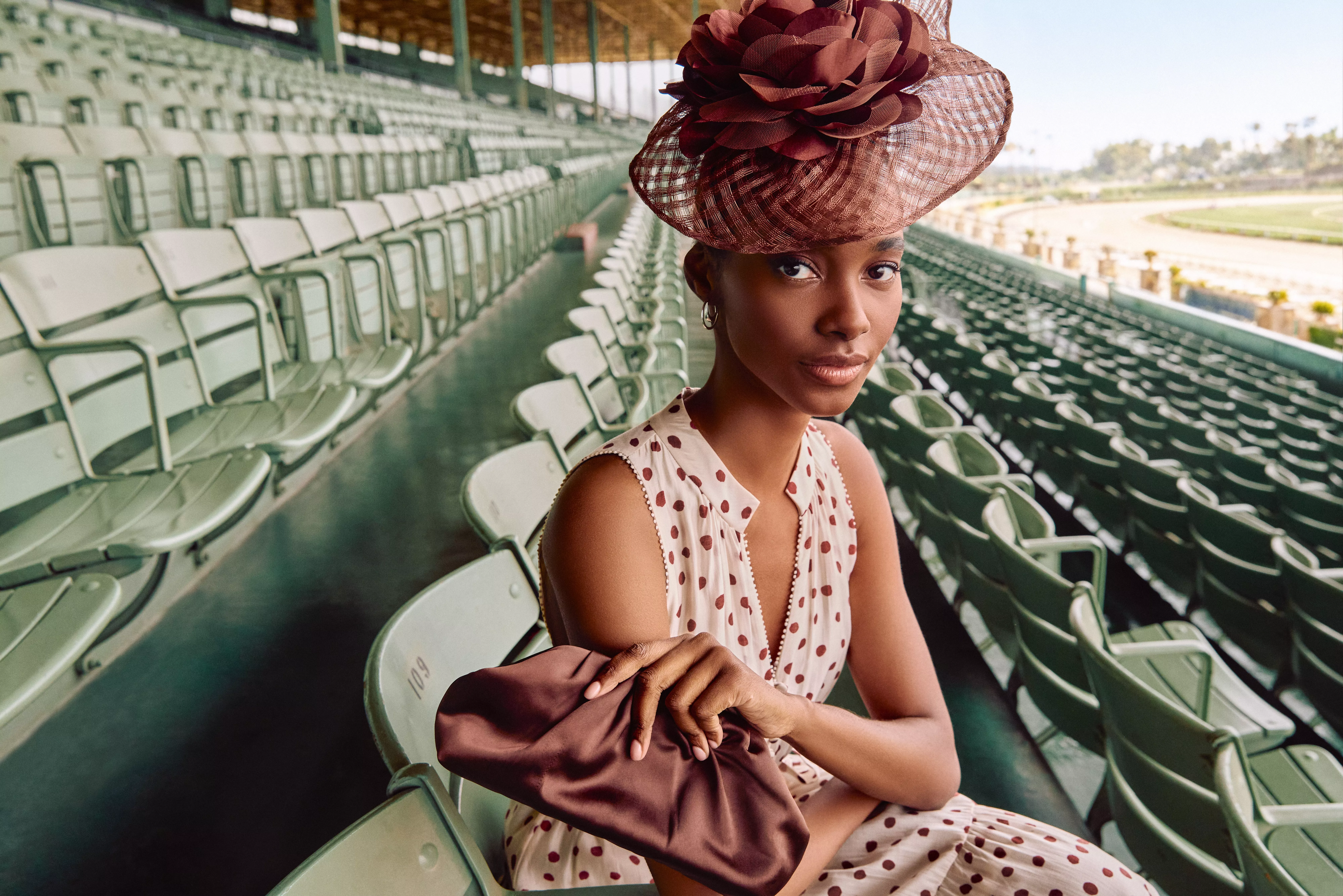 Elegant woman in polka dot dress with statement fascinator seated in empty racecourse grandstand seats