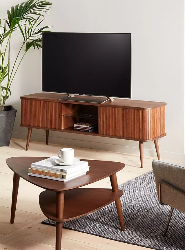 Modern flat-screen TV on mid-century wooden media unit with shelves, books, remote and plant in living room