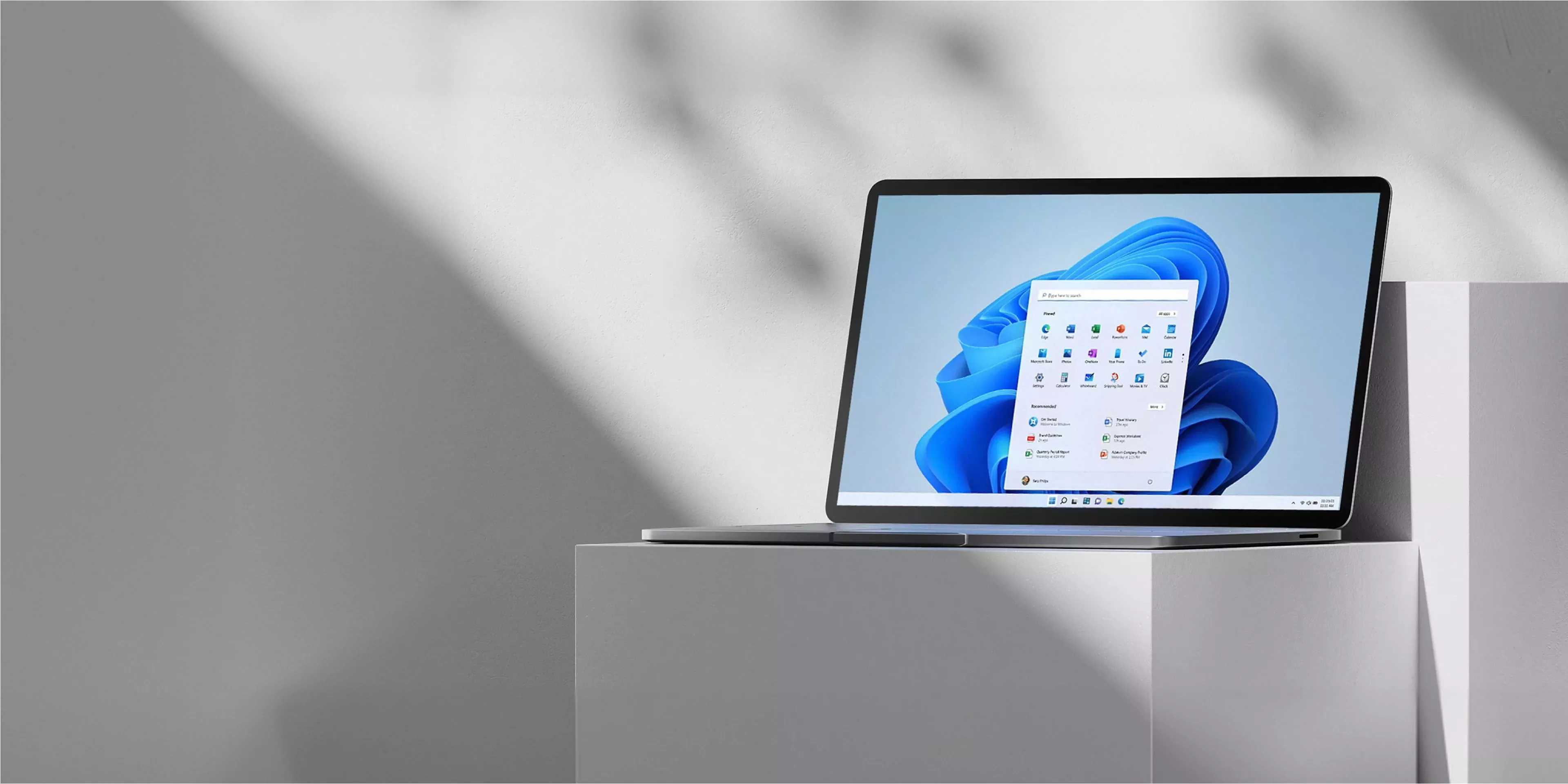 A sleek laptop on a minimalist grey surface displaying a vibrant blue abstract wallpaper on its screen.