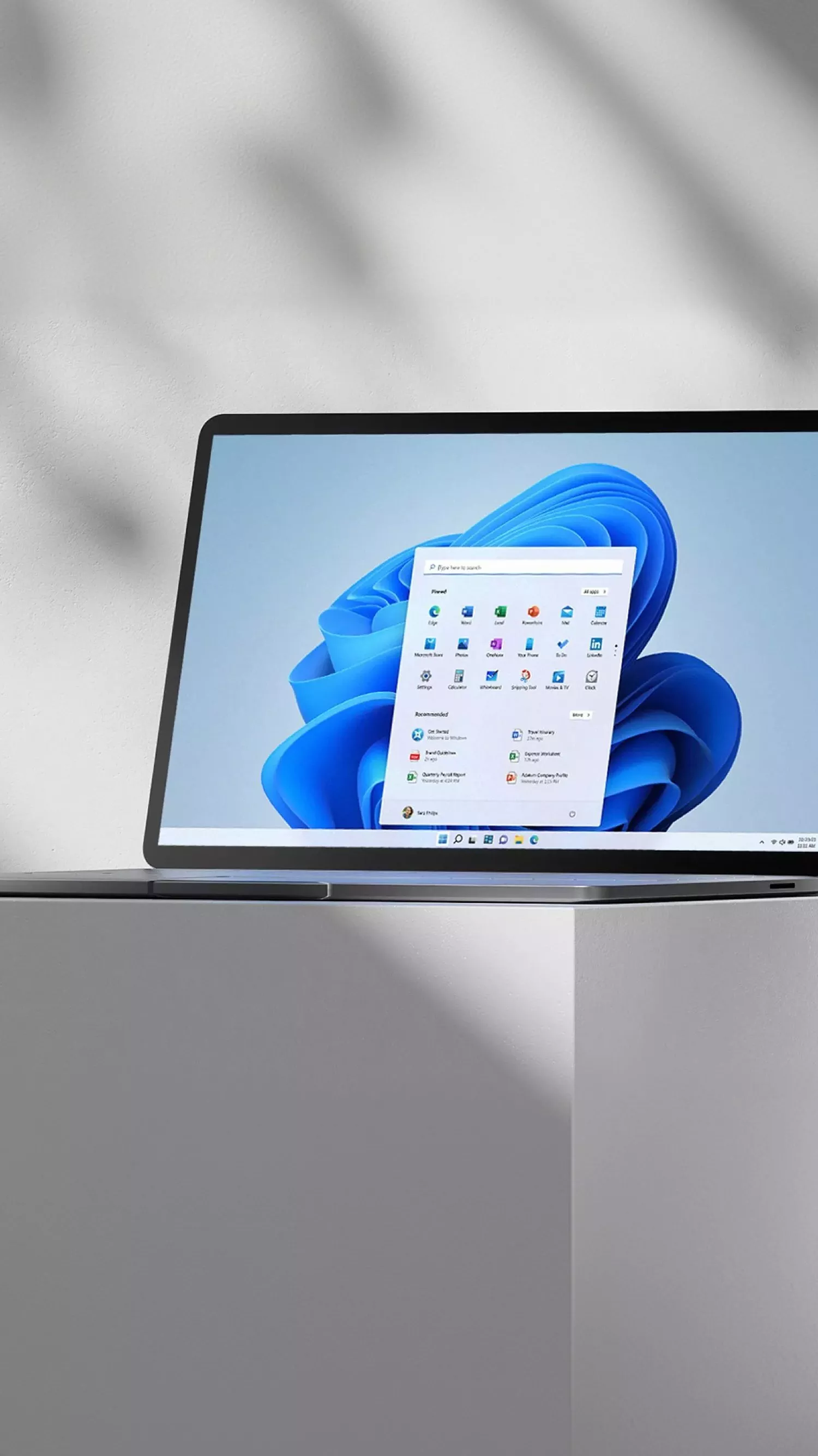 A sleek laptop on a minimalist grey surface displaying a vibrant blue abstract wallpaper on its screen.