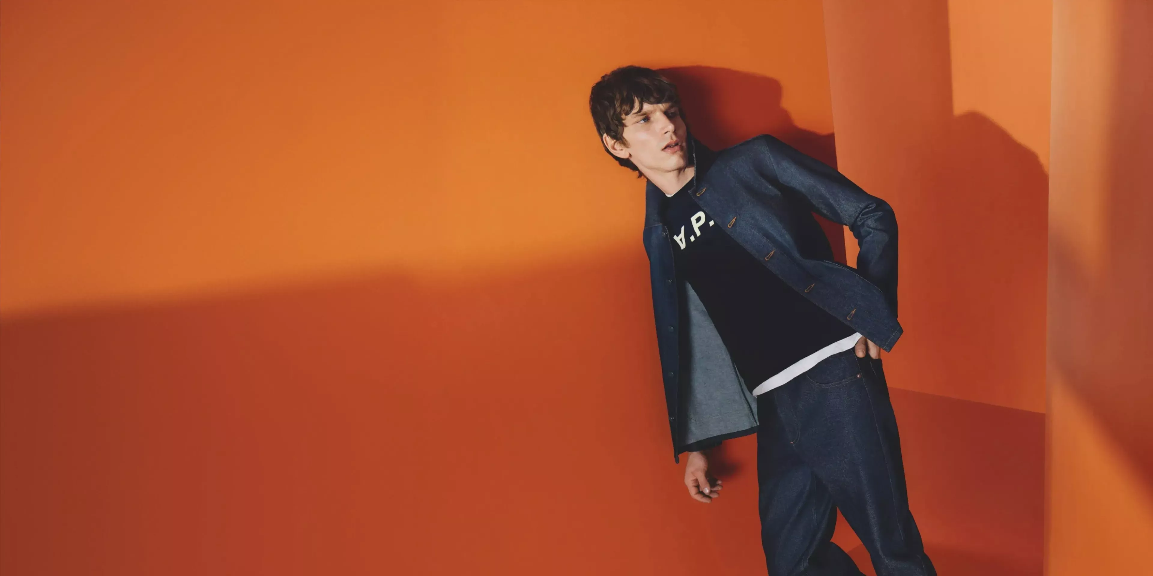man wearing APC clothes leaning on an orange wall 