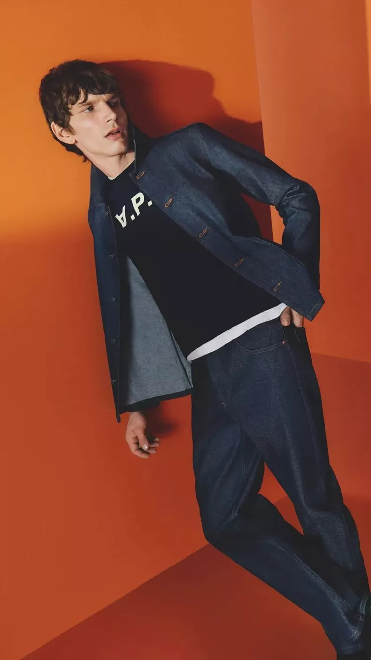man wearing APC clothes leaning on an orange wall 