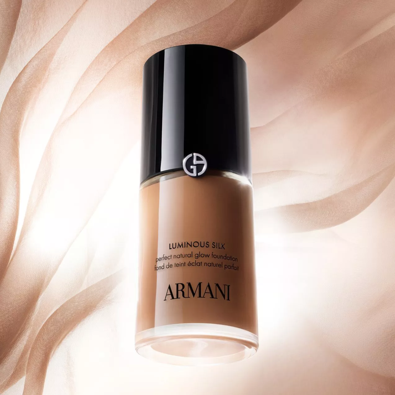 Bottle of Giorgio Armani Luminous Silk foundation set against a soft, draped, beige silk fabric background, with large white "ARMANI" text across the top.