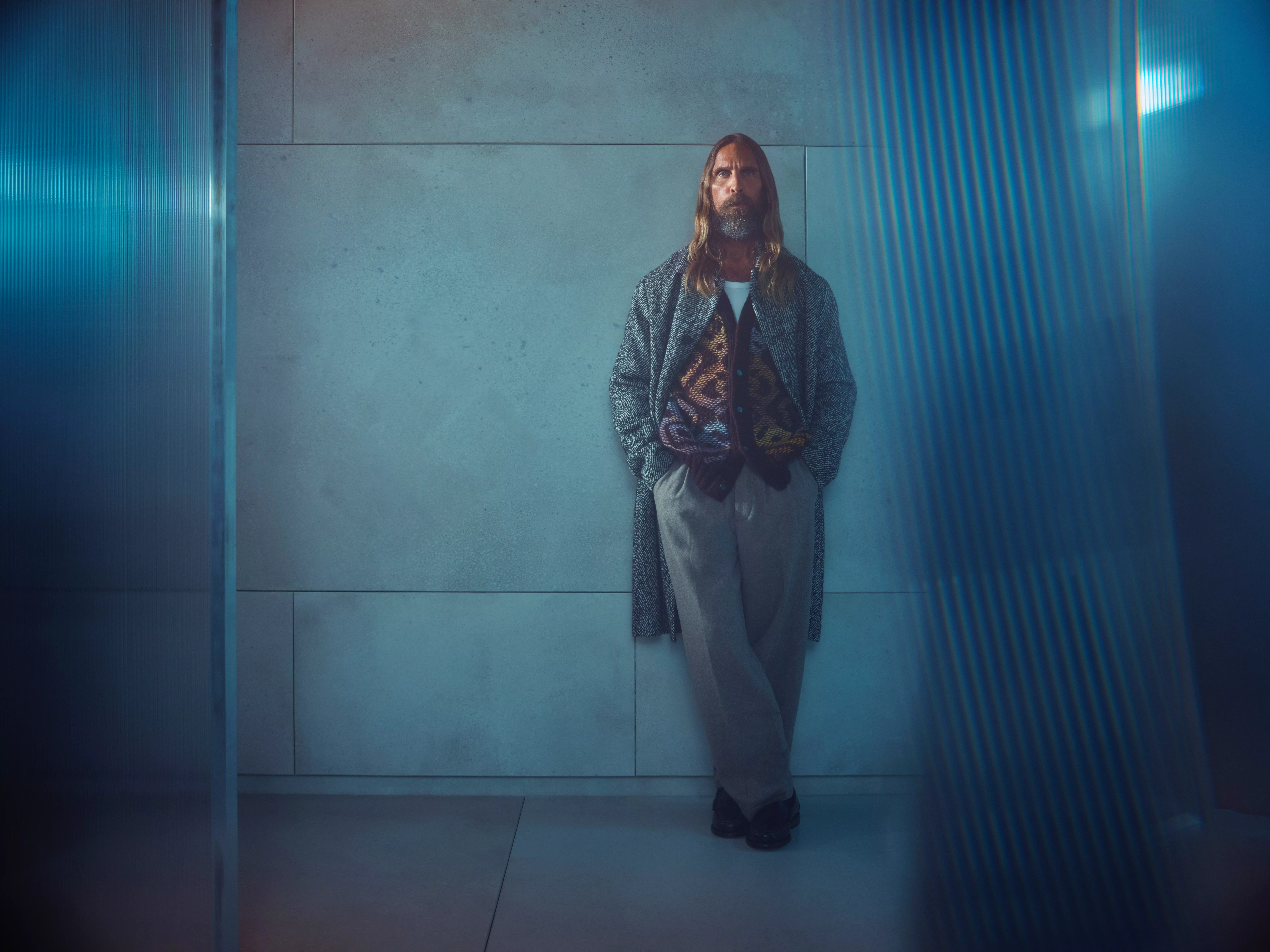 Man wearing a knitted patterned vest with tailored trousers and overcoat