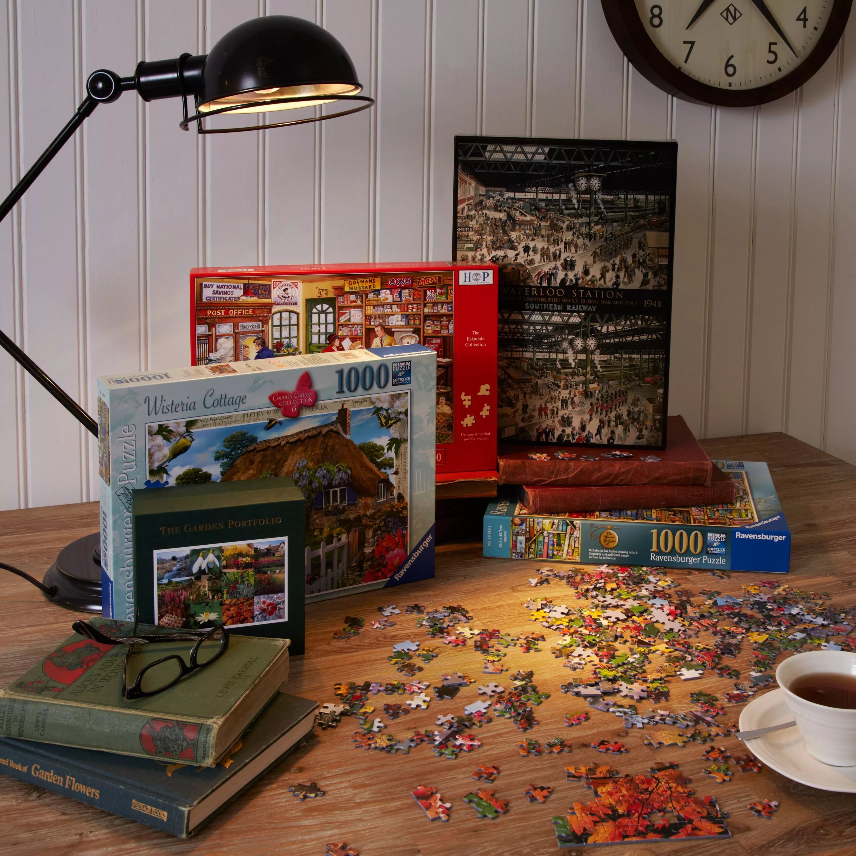 Jigsaw puzzle pieces on wooden table with 1000-piece puzzle boxes, books, desk lamp and wall clock in room