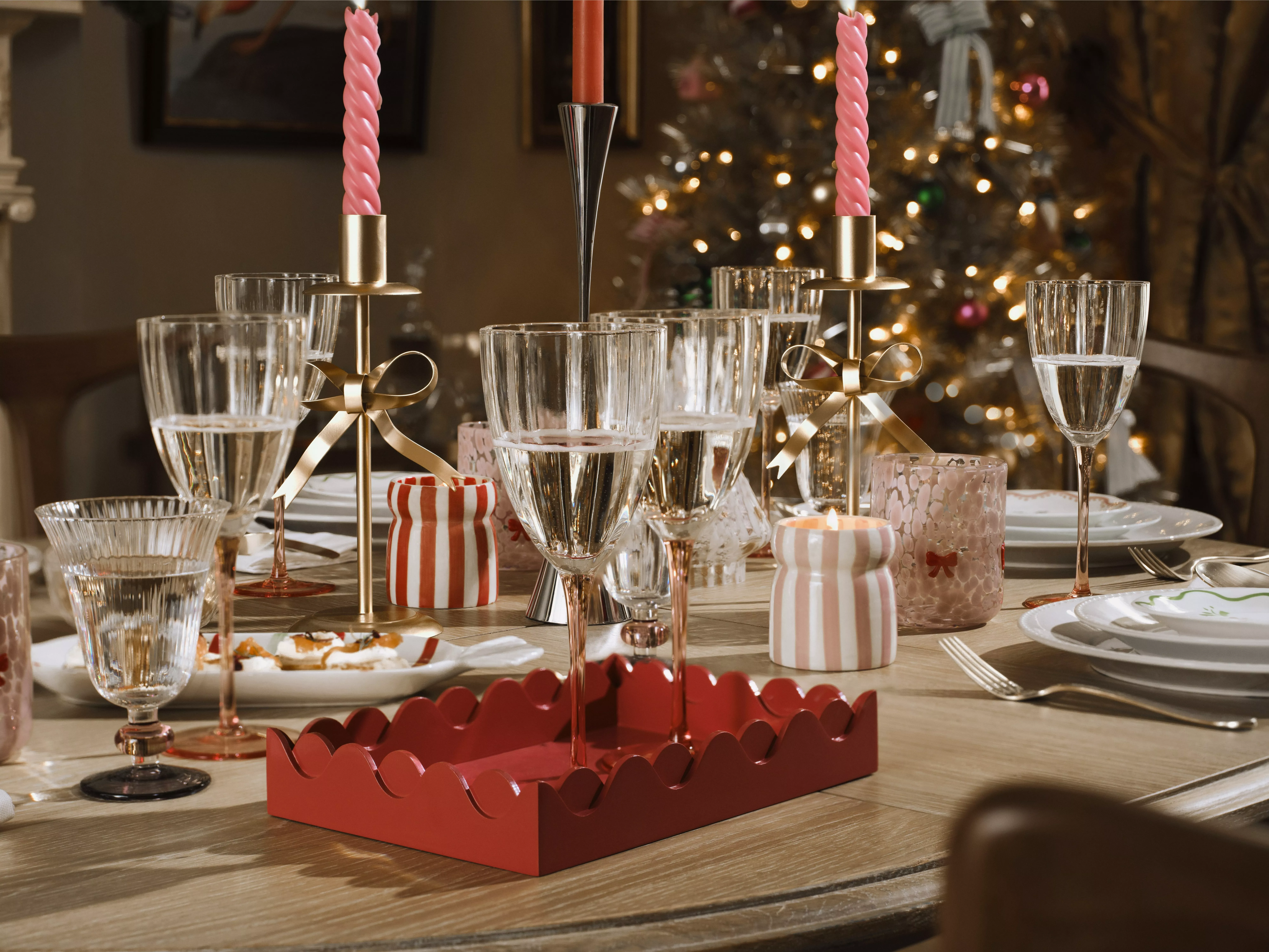 Table laid with gold bow candle sticks, glasses, plates, cutlery and candles in striped pots